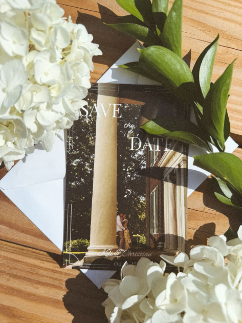 A custom Save the Date framed with flowers features an engaged couple kissing while leaned against a large white column in Chattanooga, Tennessee.