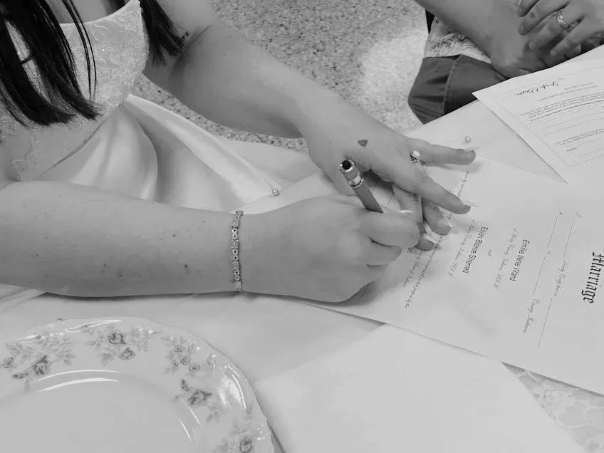 Person signing a document at a table, with a decorative plate nearby.