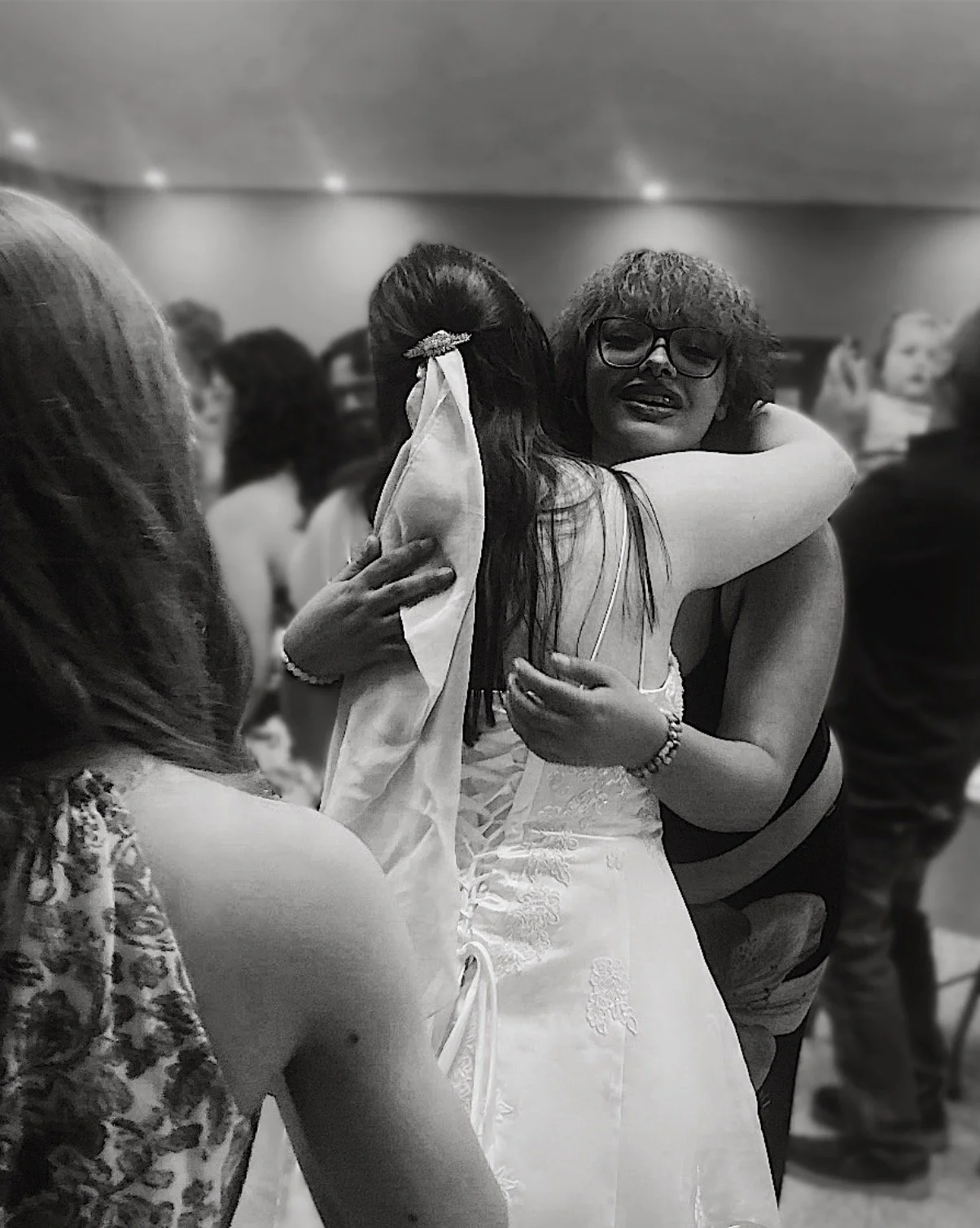 A bride in a white ballgown style wedding gown hugs her guest a crowded wedding reception in New Castle, Indiana.