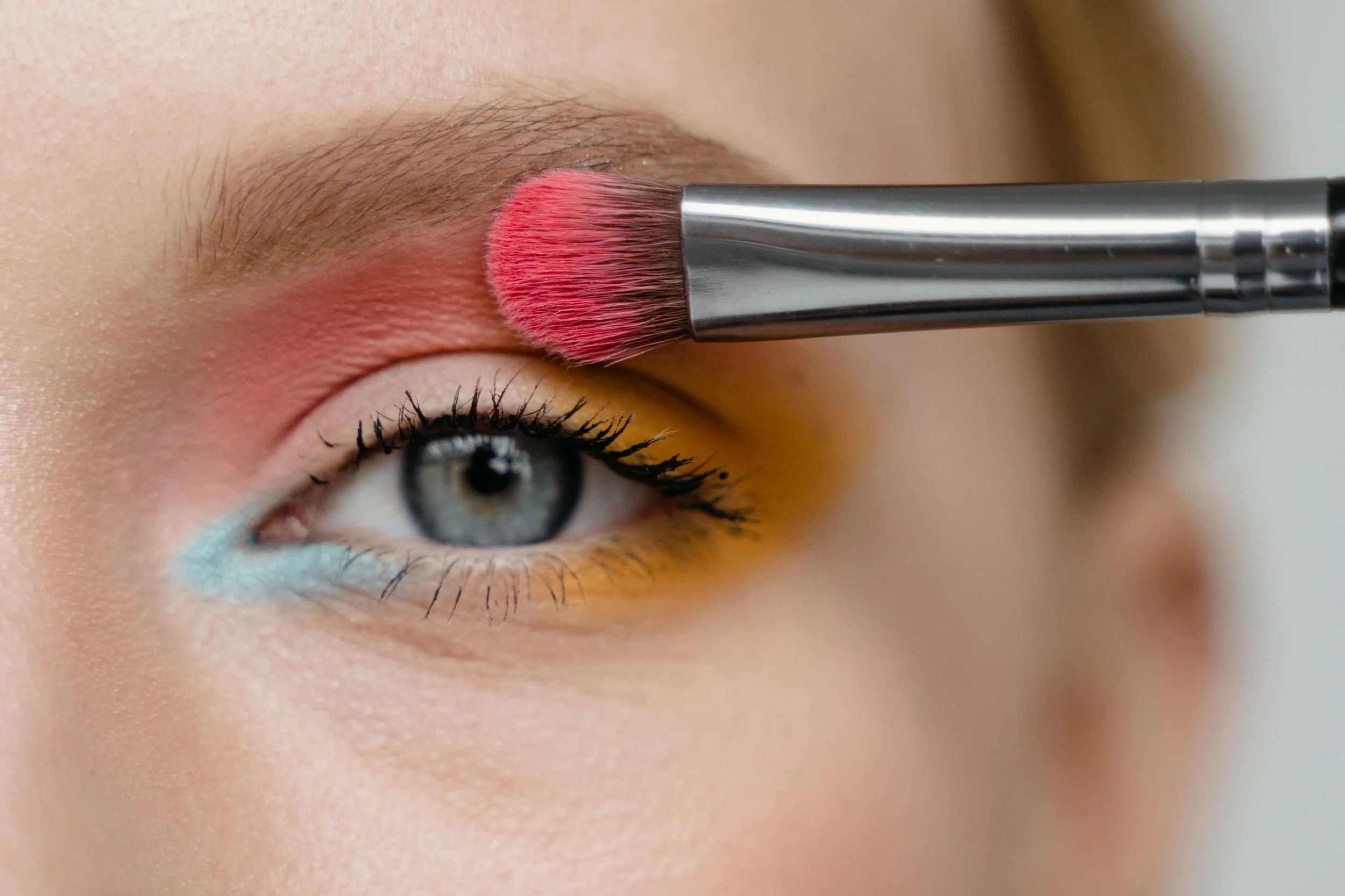 Een close-up foto van een oog waarbij make-up wordt aangebracht met een borsteltje op de ooglid.