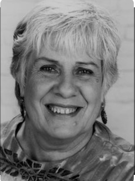 A smiling woman with short, light-colored hair and earrings, wearing a patterned top.