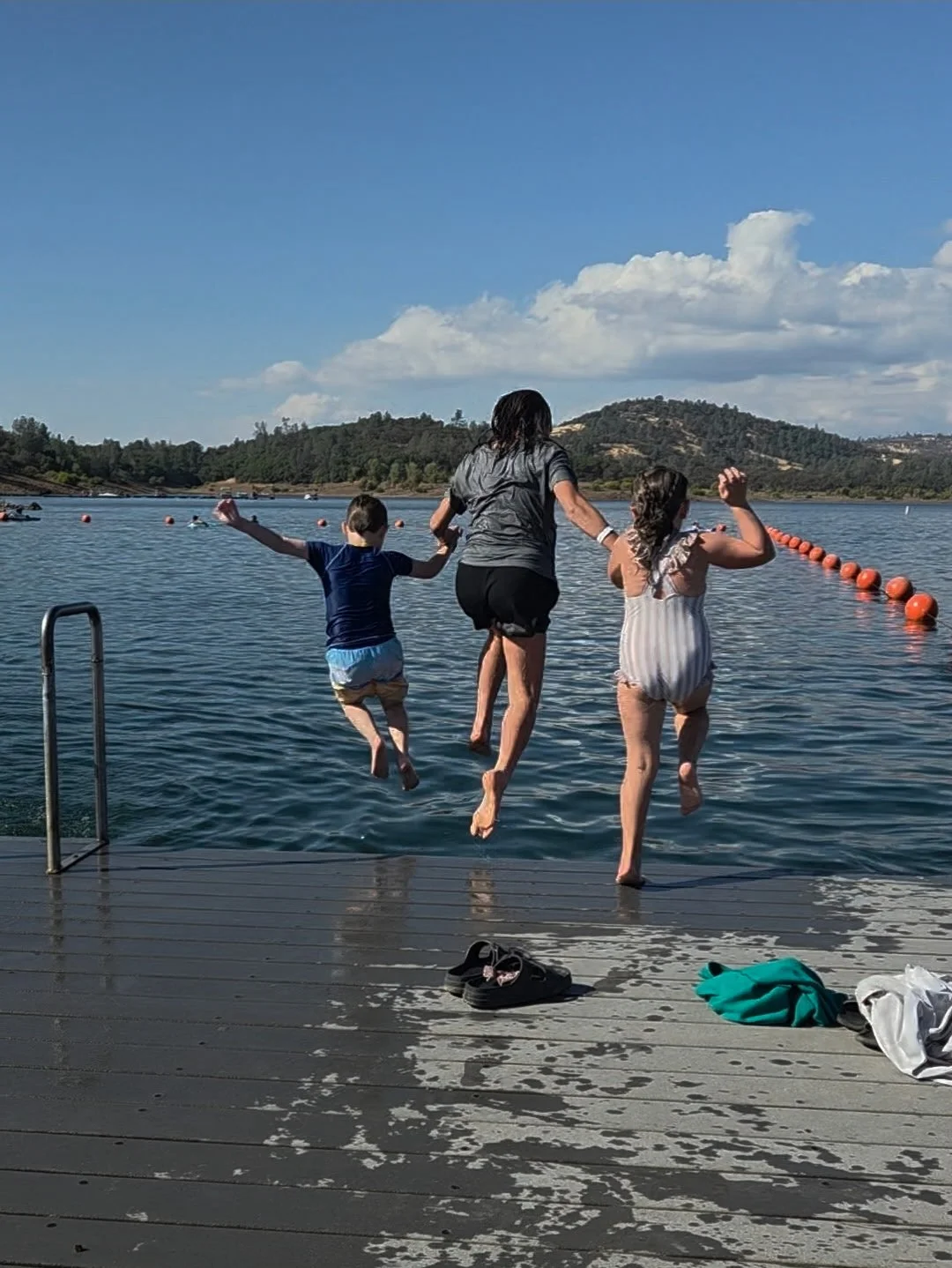 A woman and two children jumping into a lake from a dock on a sunny day.