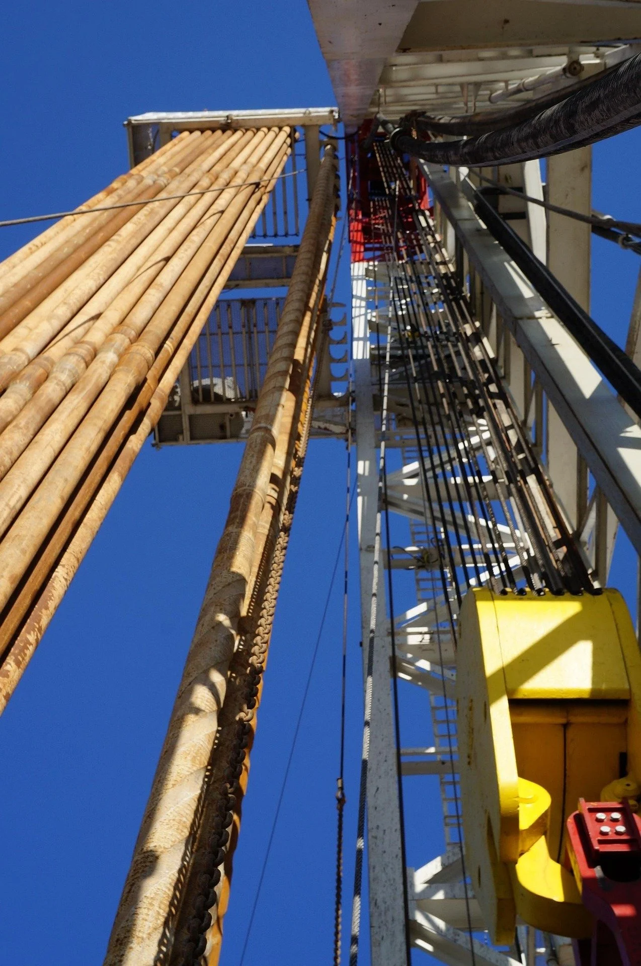 Looking up at a tall industrial structure with metal pipes, ladders, and safety railings against a clear blue sky.