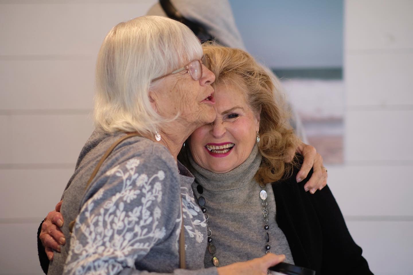 Two elderly women sharing a joyful hug, smiling and embracing each other.