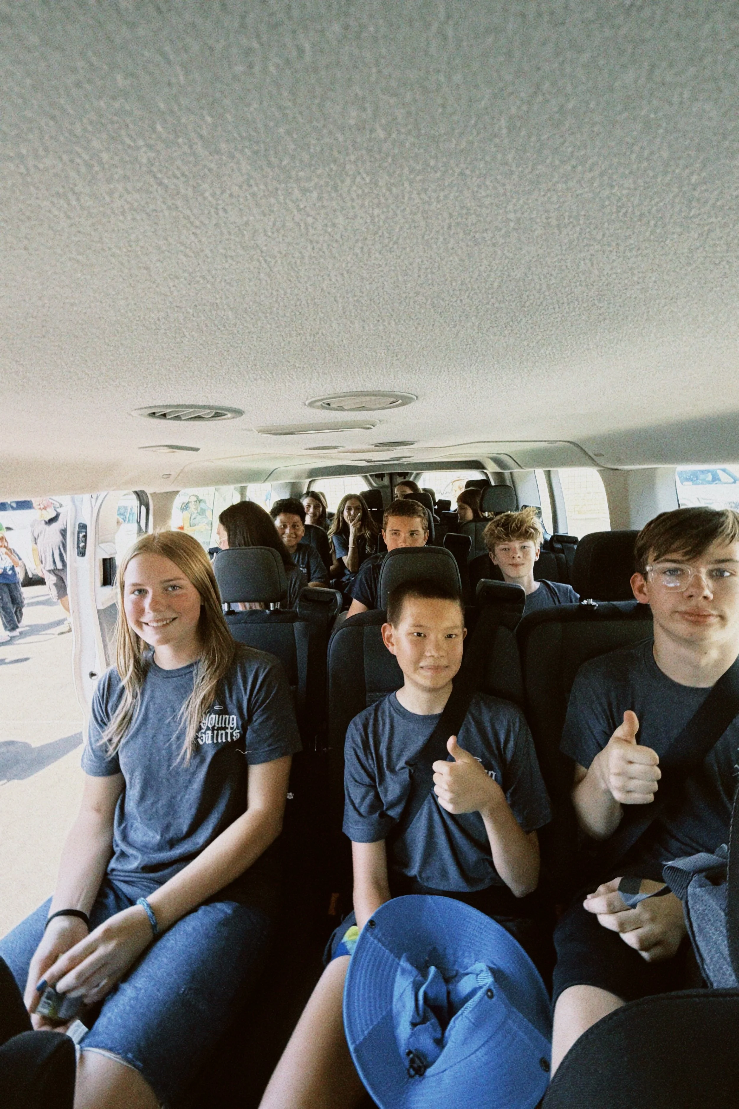 Group of young students sitting inside a bus with some giving thumbs up.