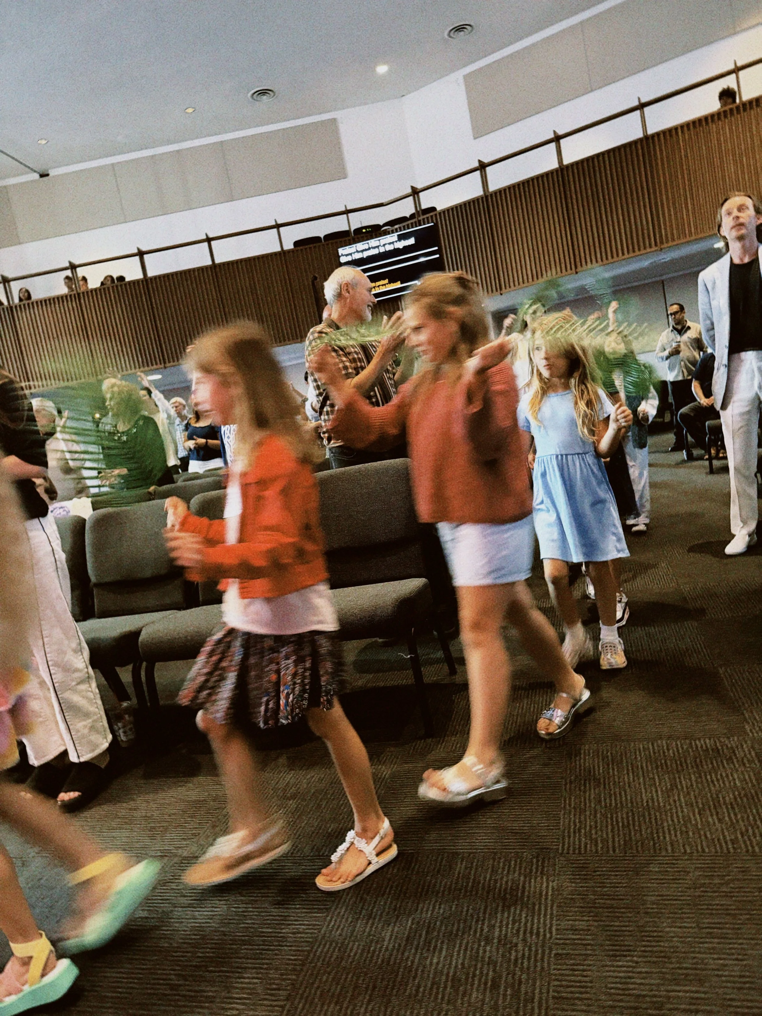 People walking in an indoor space, possibly a waiting area or lobby, with some seated and others standing or walking.