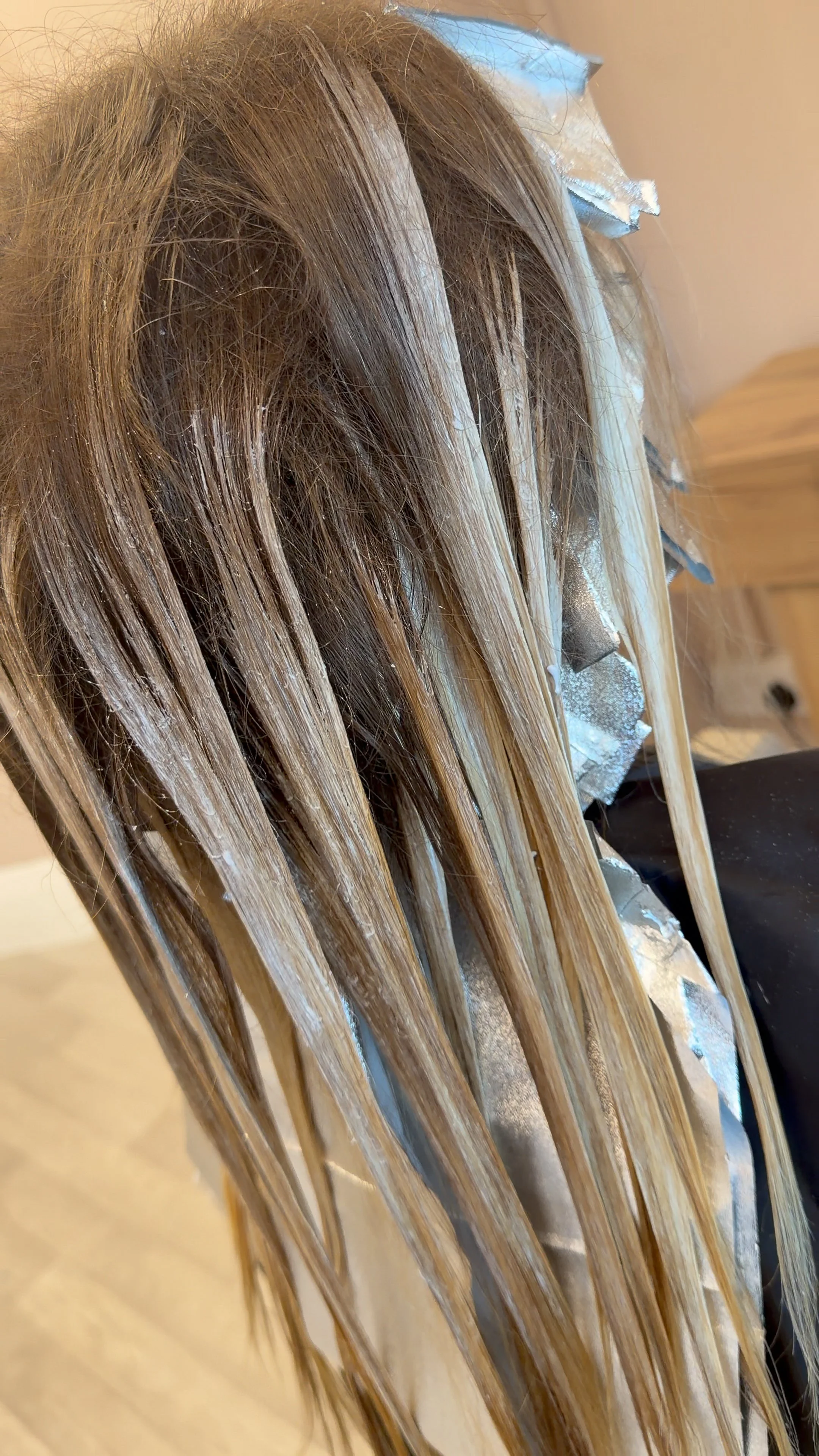 Hair coloring process in progress, with blonde hair sections separated and foil highlights being applied.