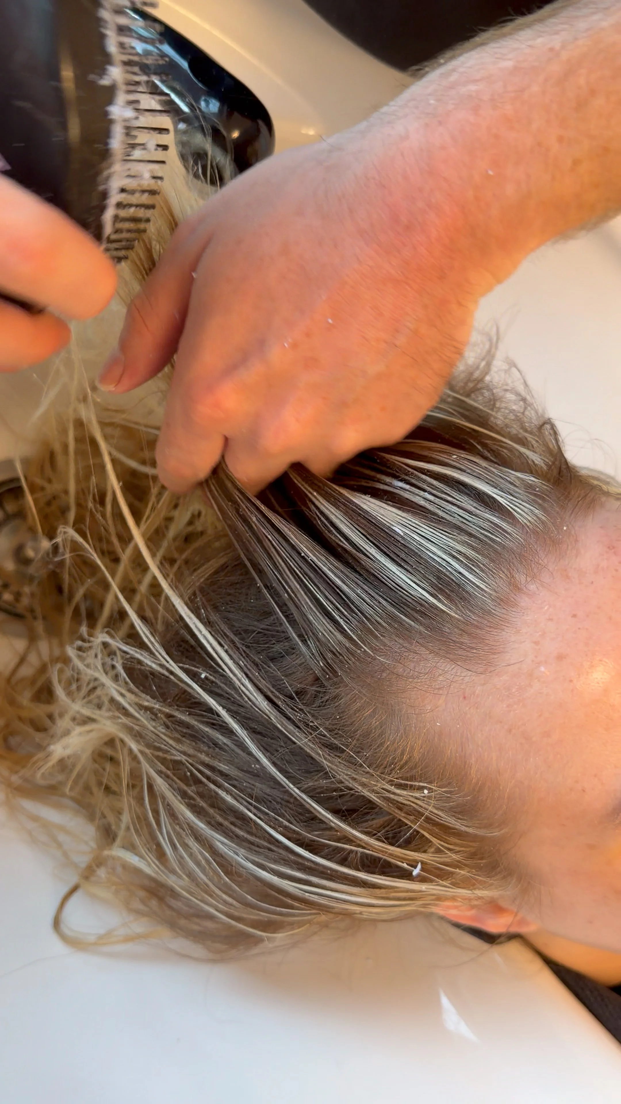 Close-up of a person's head during a haircut with hair dye or bleach being applied to the hair.