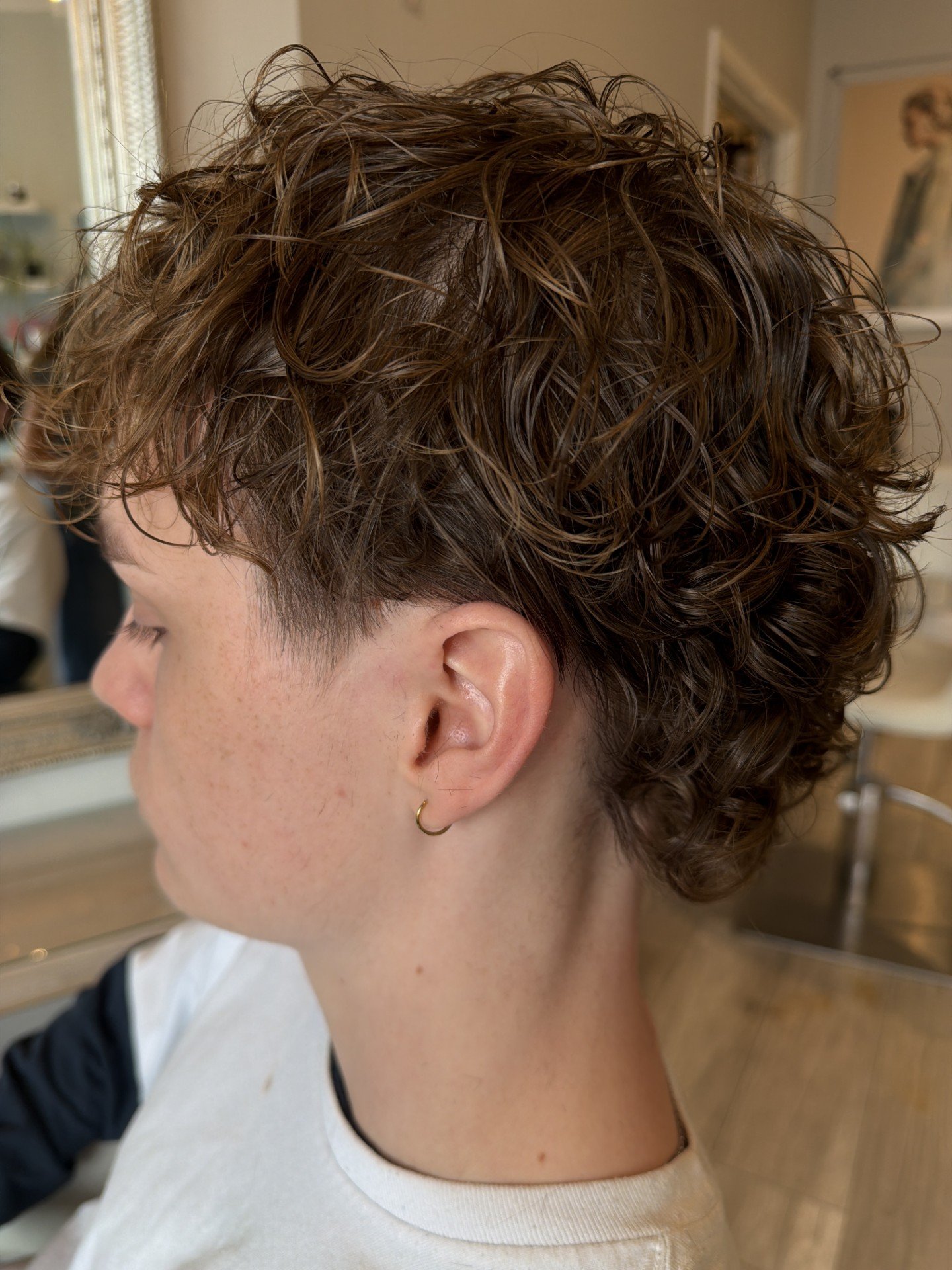 Side view of a person with short, curly, brown hair, wearing a white and black top and a small gold hoop earring.