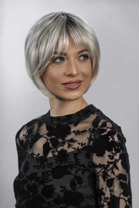 A woman with a short, layered silver-blonde bob hairstyle, wearing a black lace top with floral patterns, looking slightly to her right against a plain light gray background.