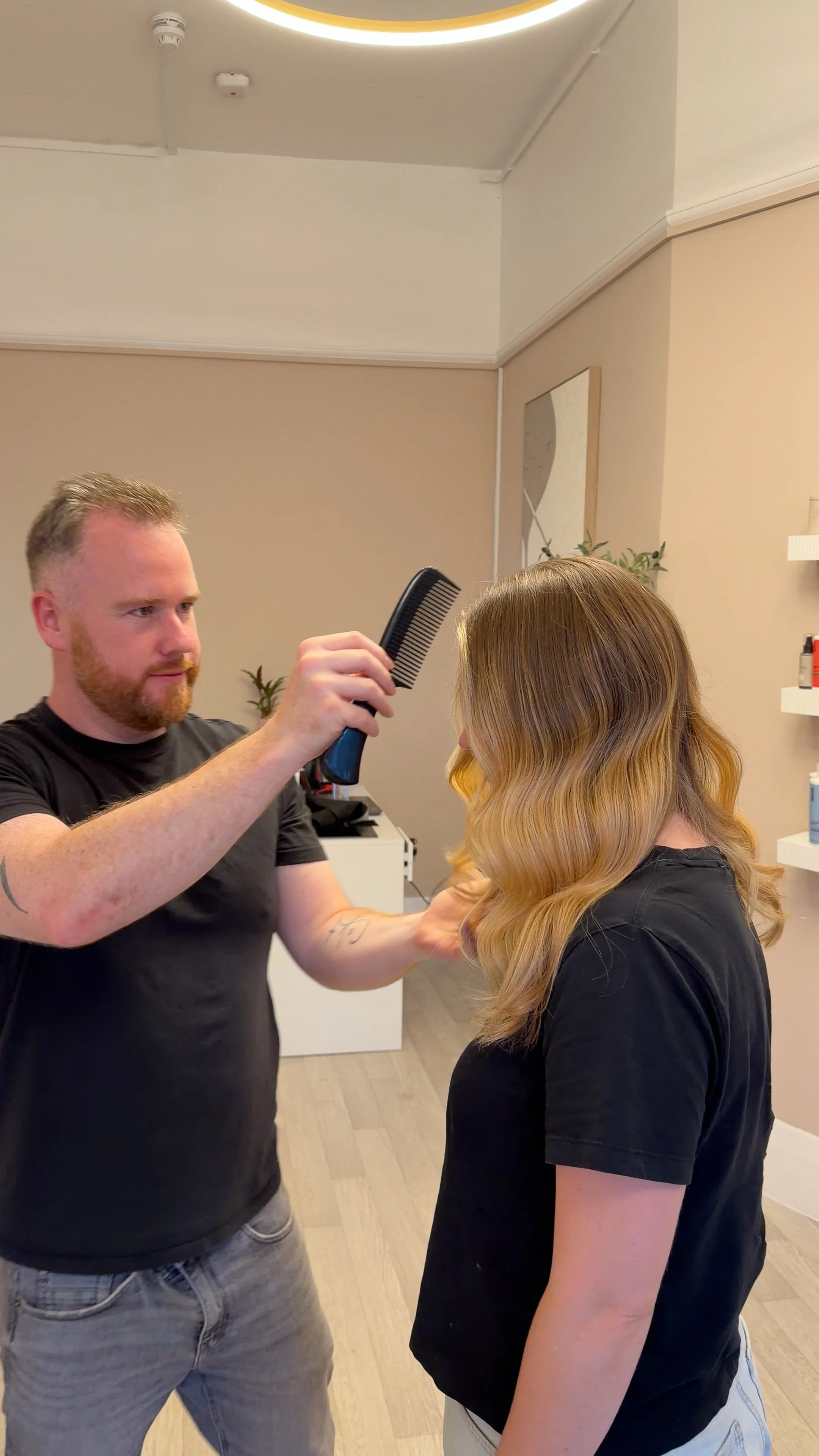 A hairstylist drying a woman's hair with a blow dryer in a salon.