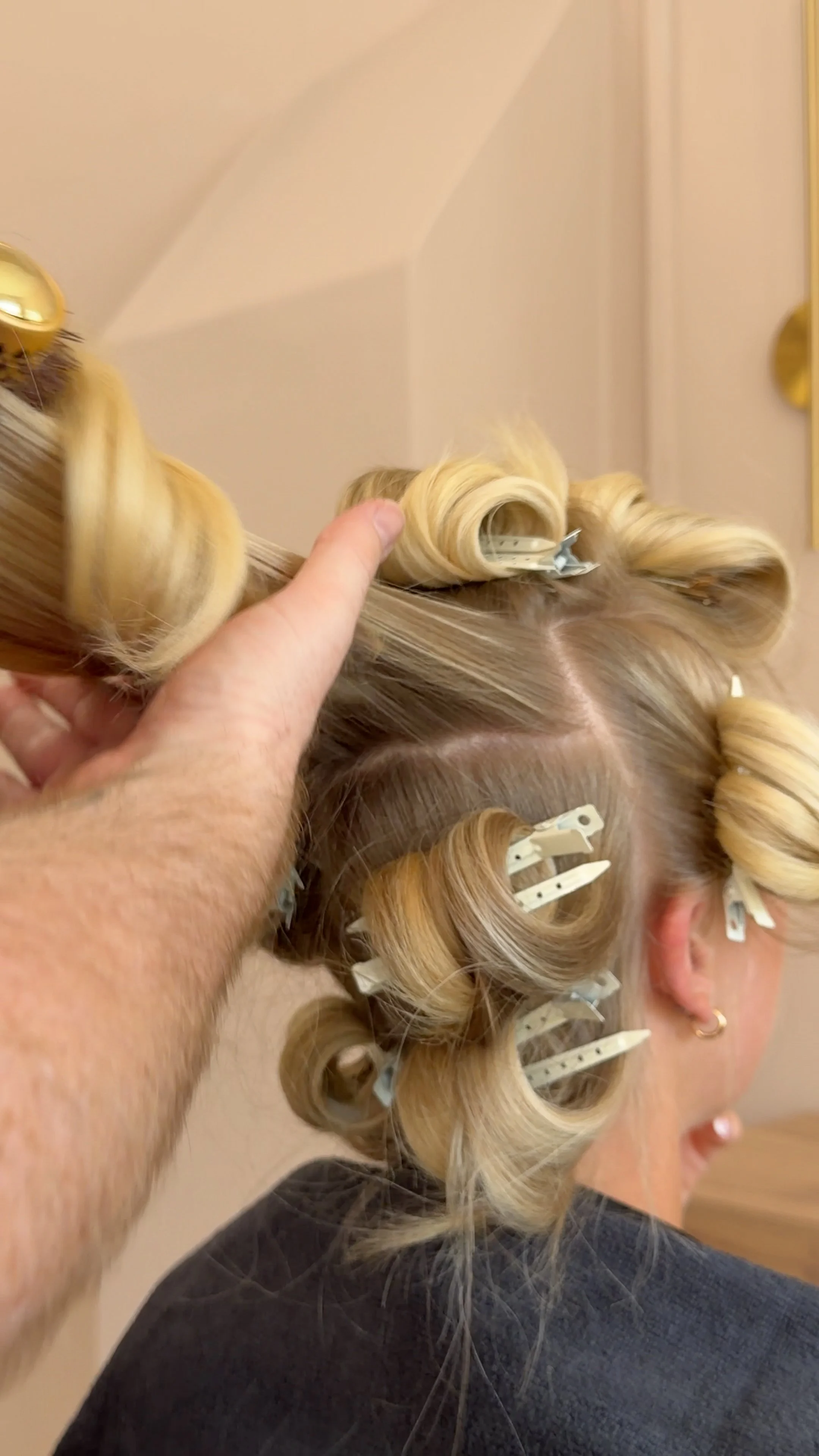 A person with blonde hair in curlers is having their hair styled, with another person's hand adjusting one of the curlers.