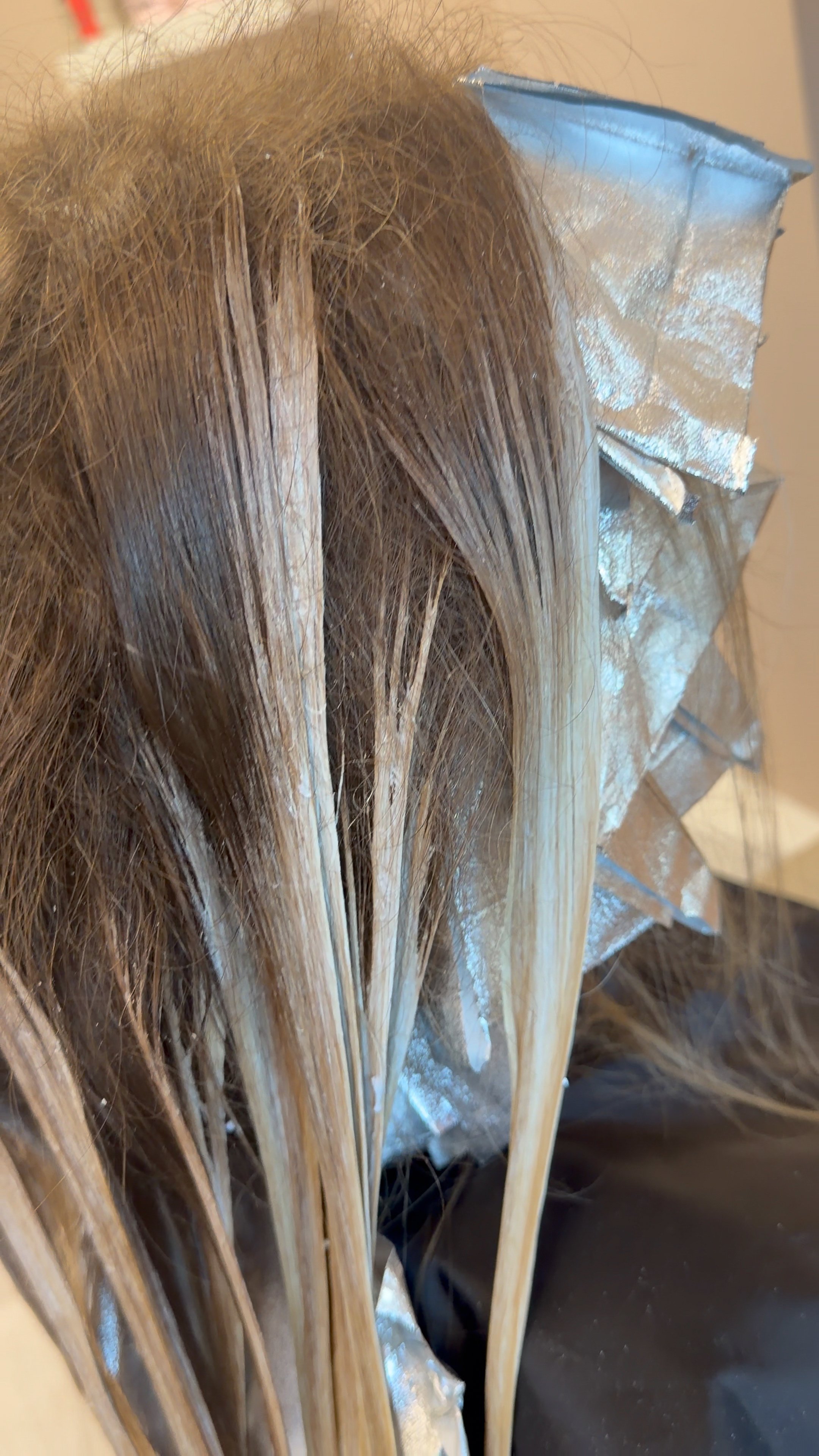 Close-up of brown hair with aluminum foil highlights used for hair coloring.