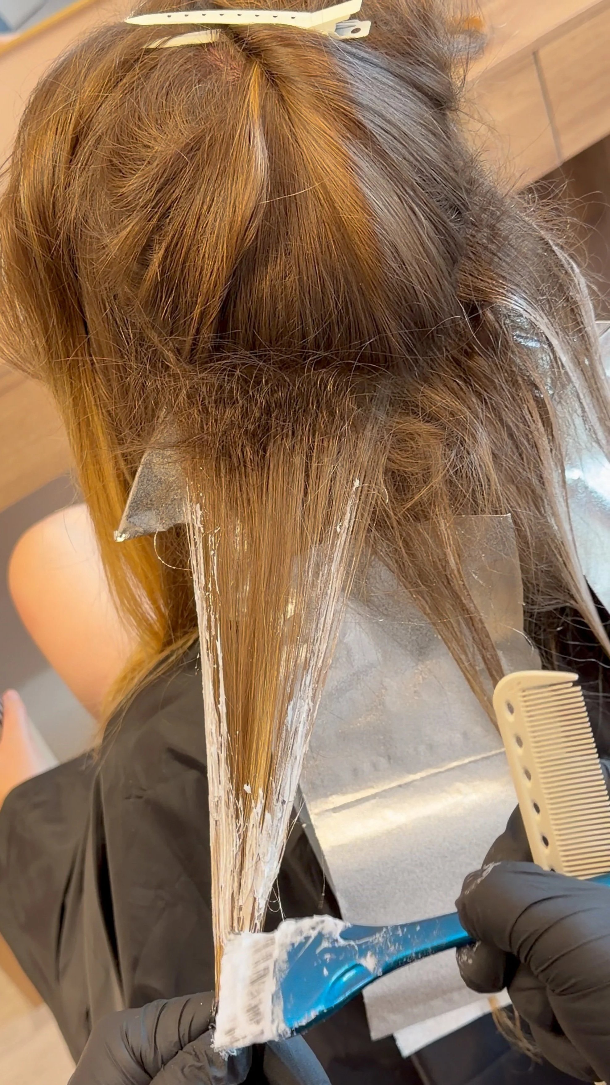 Hairdresser applying bleach or lightener to a customer's hair using a hairbrush and foil at a salon.