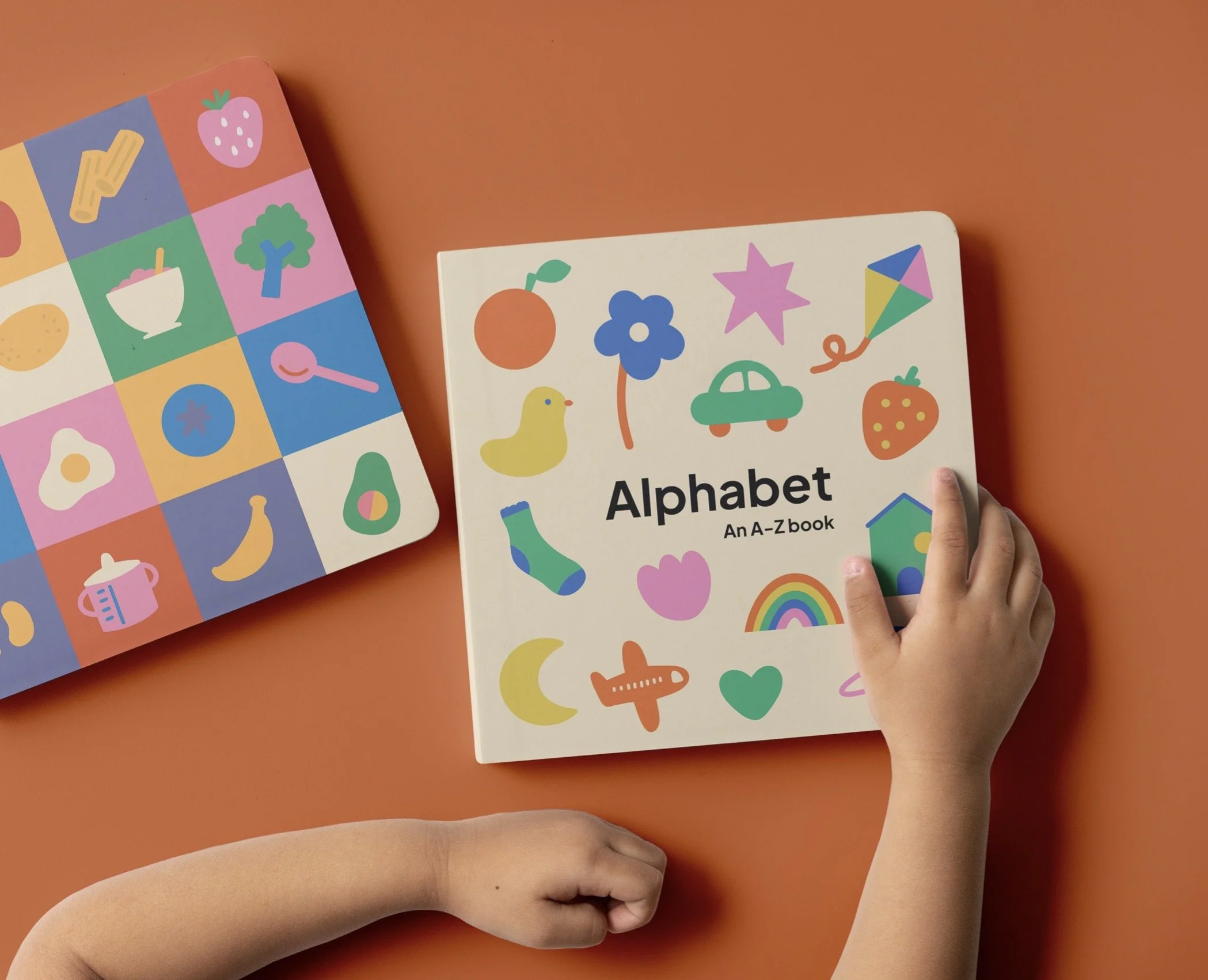 Children holding a colorful alphabet book with animal and fruit illustrations, on an orange background.