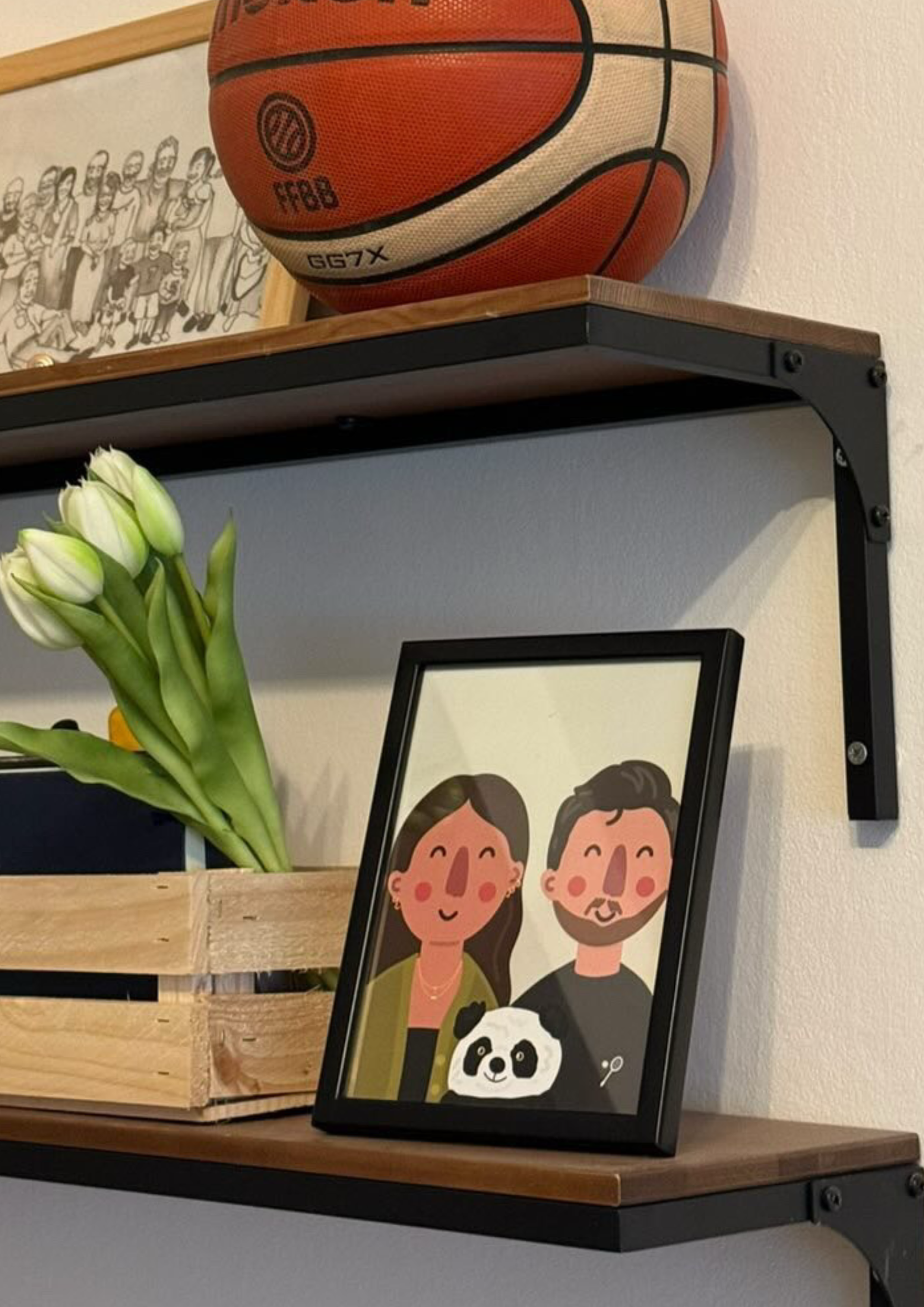 A basketball on a wooden shelf, a framed cartoon illustration of smiling people, a bouquet of white tulips, and another framed picture with a panda bear on a table.