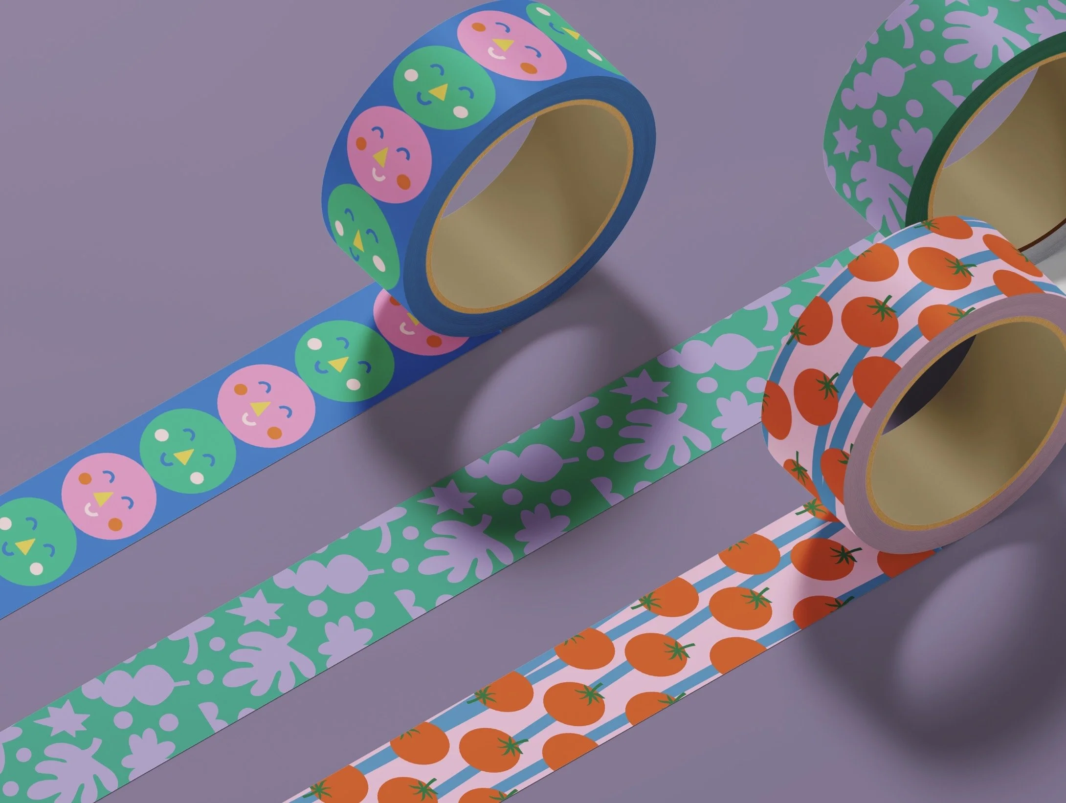 Three rolls of decorative tape with colorful patterns. The first tape has a pattern of pink and green faces with happy expressions on a blue background. The second tape has a snowflake design in shades of purple on a green background. The third roll 