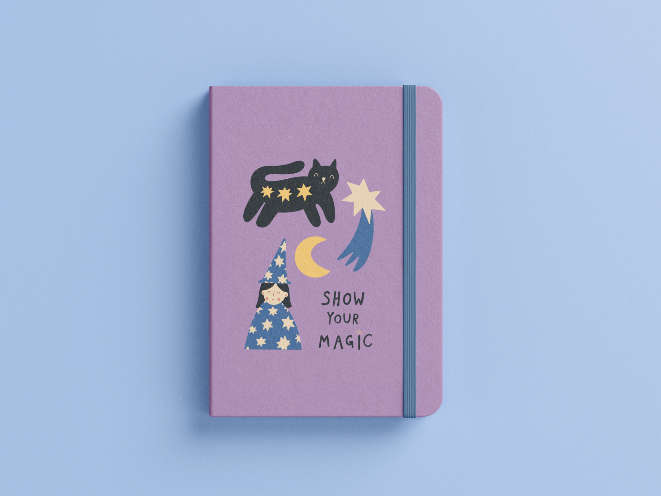 A pink notebook with a black cat illustration, stars on its body, and the phrase "Show Your Magic" with a wizard hat and moon design on a light blue background, secured with a blue elastic band.