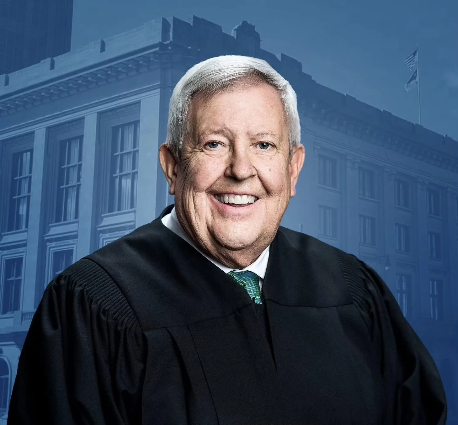 A portrait of an older man with white hair, wearing a black judicial robe, smiling in front of a blue background with a faint image of a building and American flags.