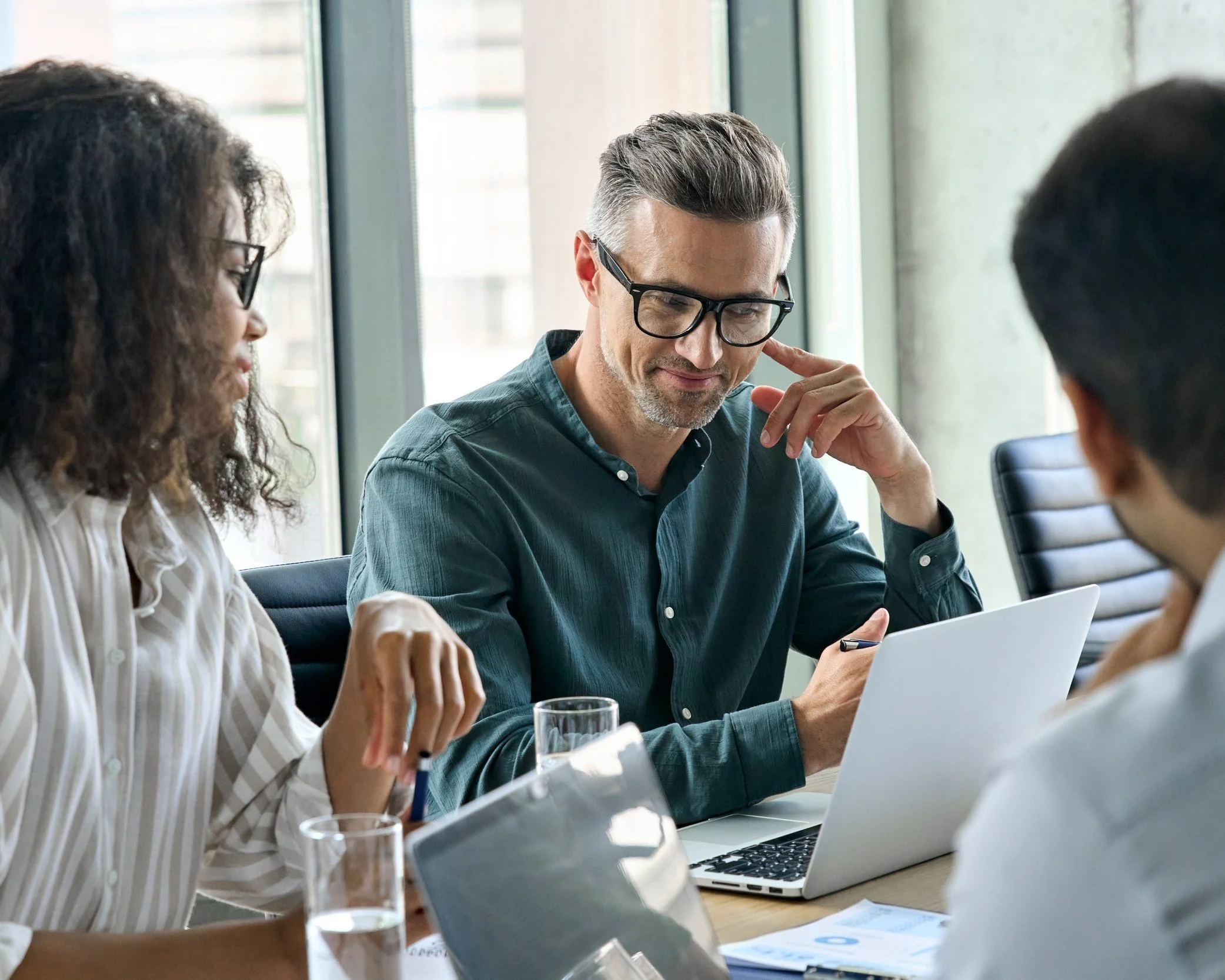 A diverse group of people sitting at a table during a business meeting or discussion in a modern office space.