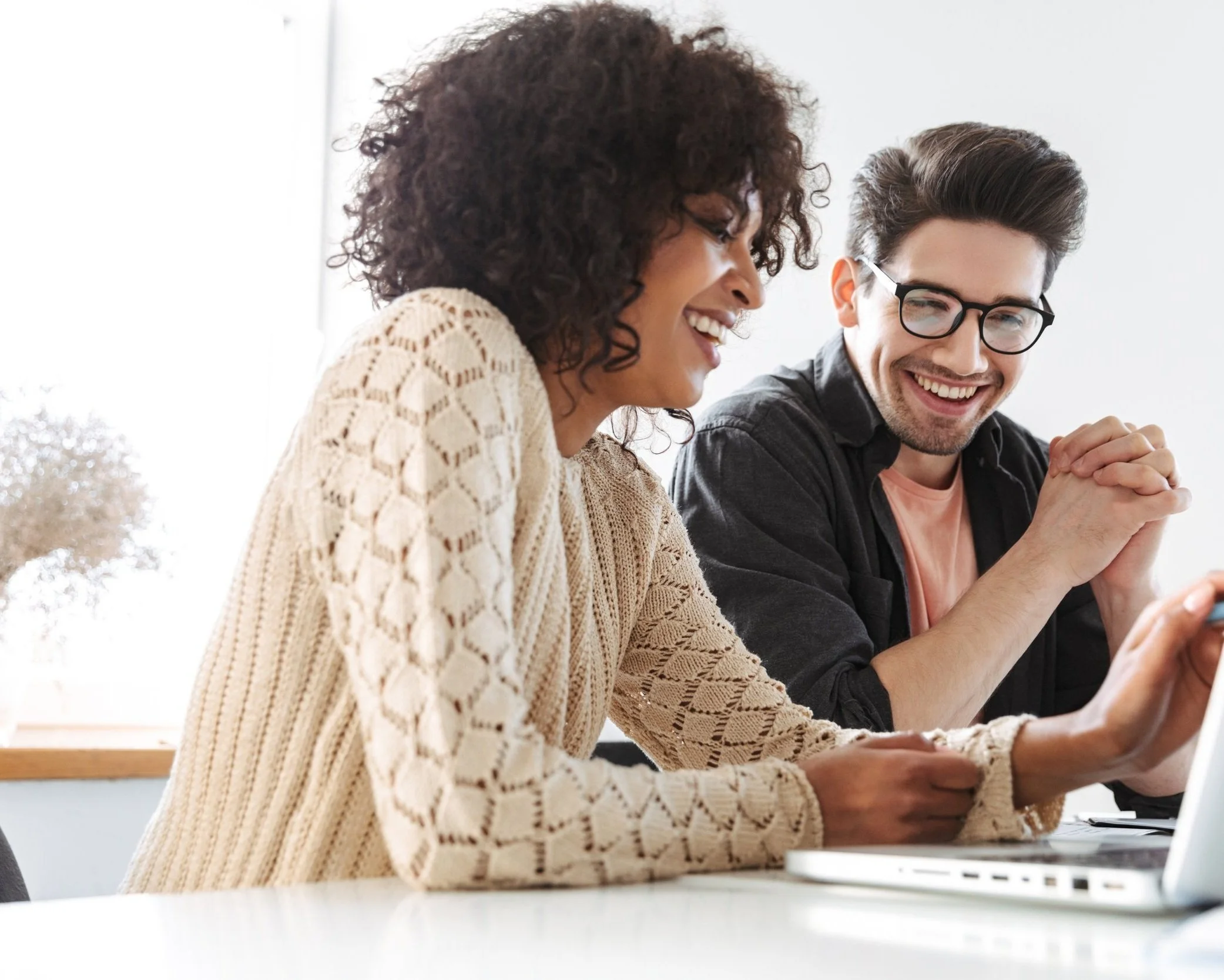 Two people sitting at a desk, smiling and working together on a laptop.