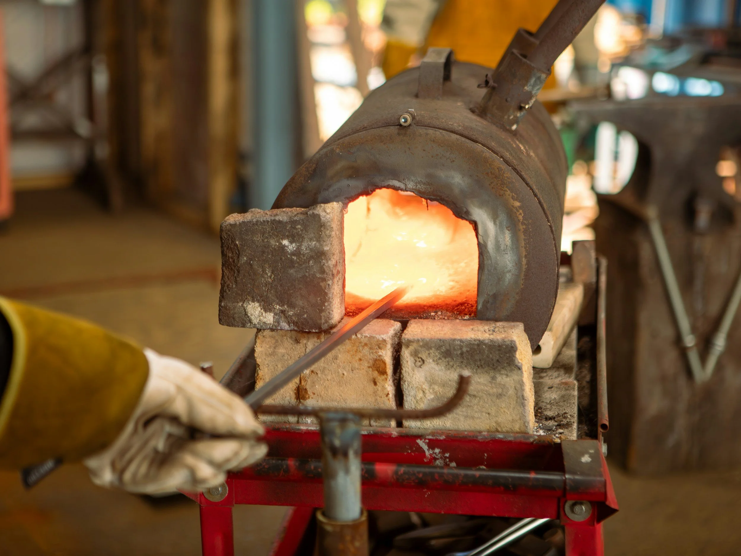 A forge or furnace with bright glowing metal inside, used for heating metal to high temperatures for shaping or welding, situated in a workshop or industrial setting.