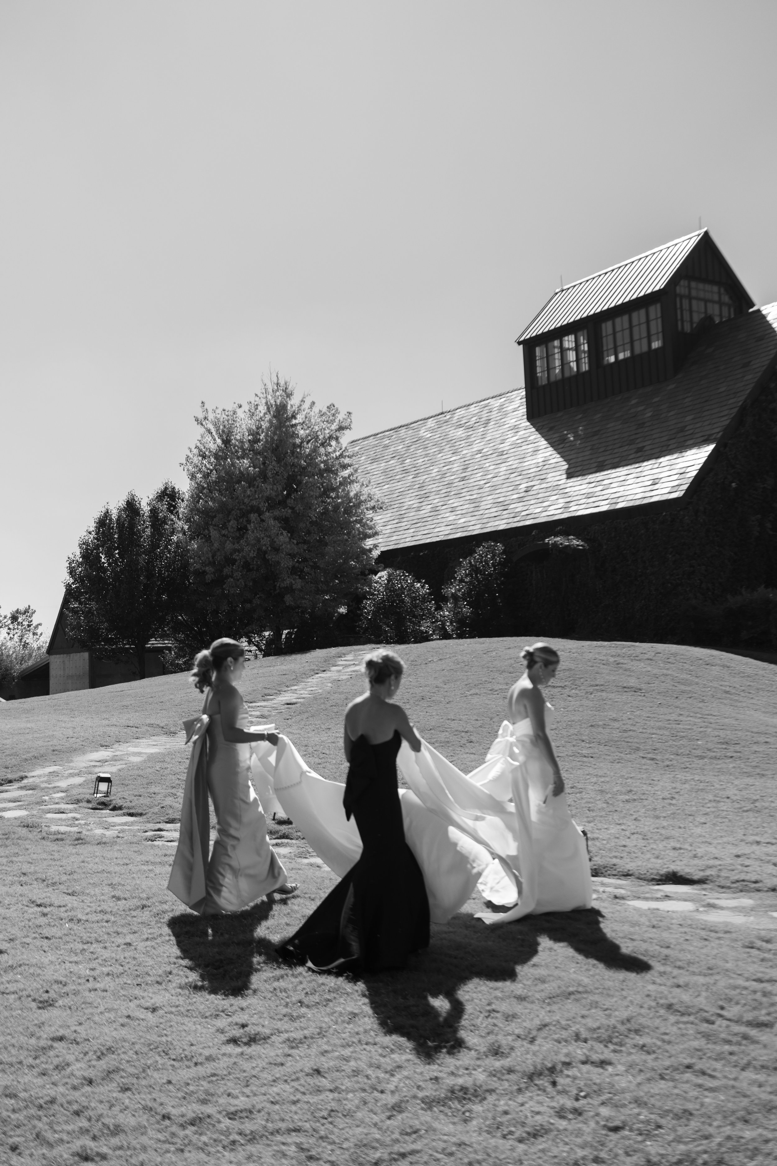 Black and white image of bridesmaids walking carrying brides train
