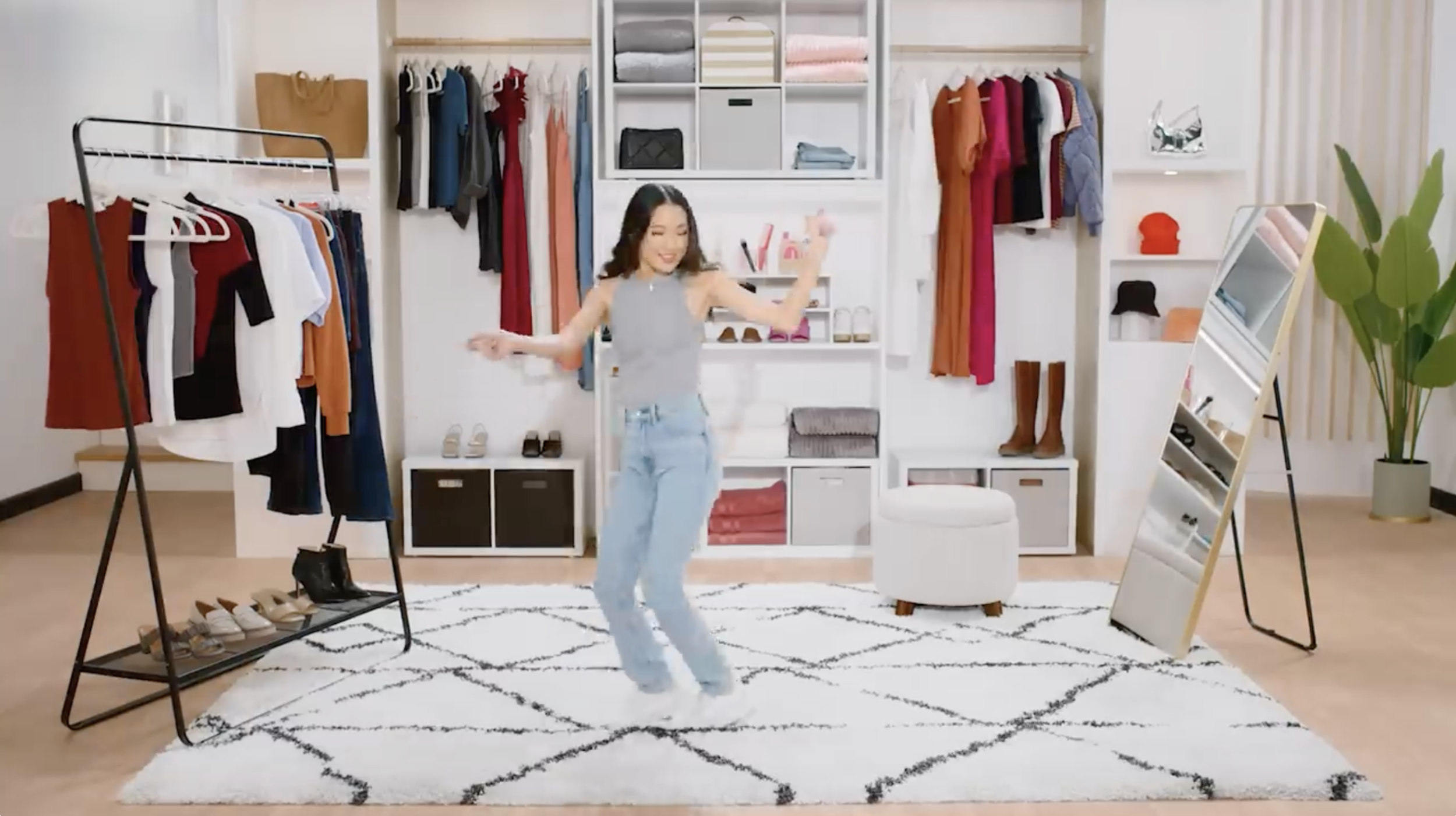 A woman dancing in a walk-in closet with clothes, shoes, and a mirror.