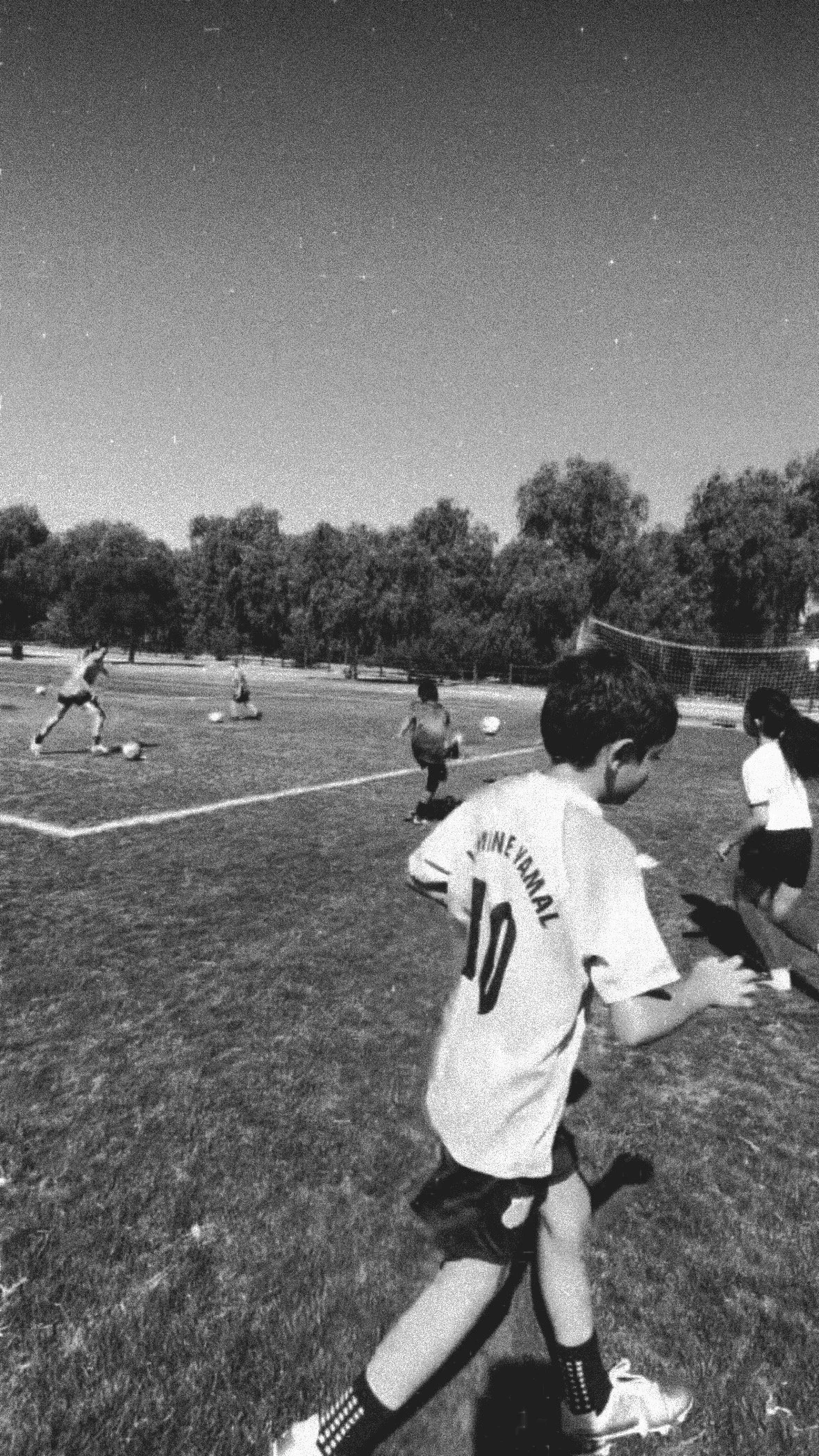 Children practicing soccer on a field at night, with trees in the background and stars visible in the sky.