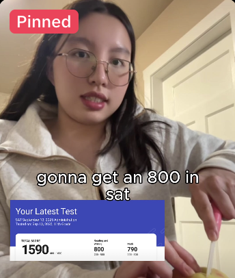 Young woman with glasses holding a phone showing a test score in front of a door.