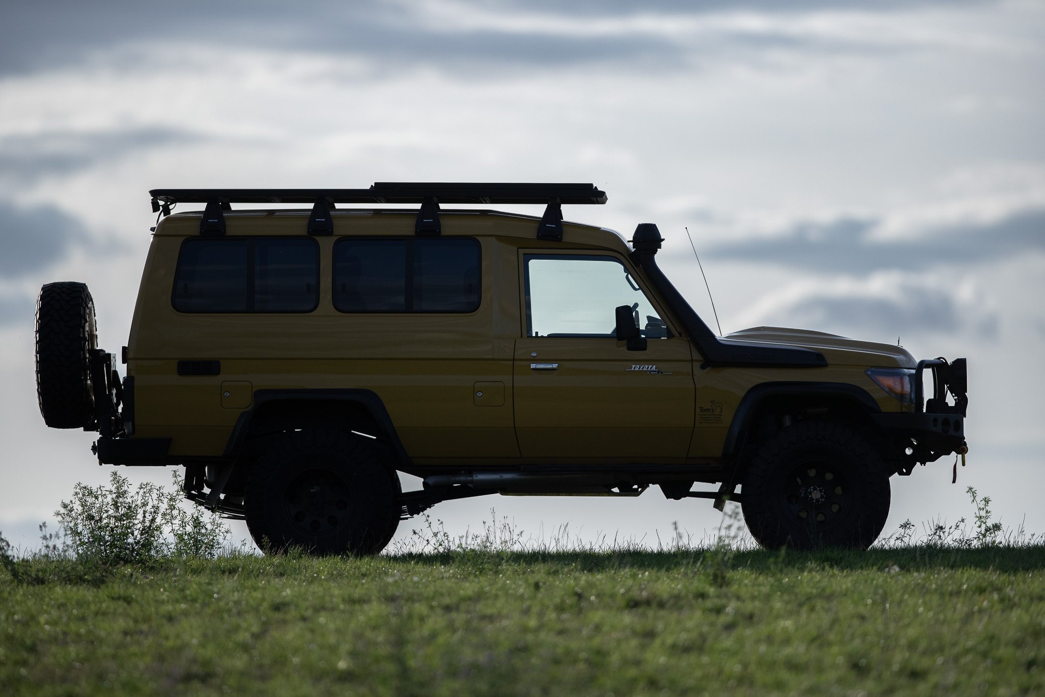 Silhouette of a yellow off-road vehicle parked on a grassy field with a cloudy sky in the background.