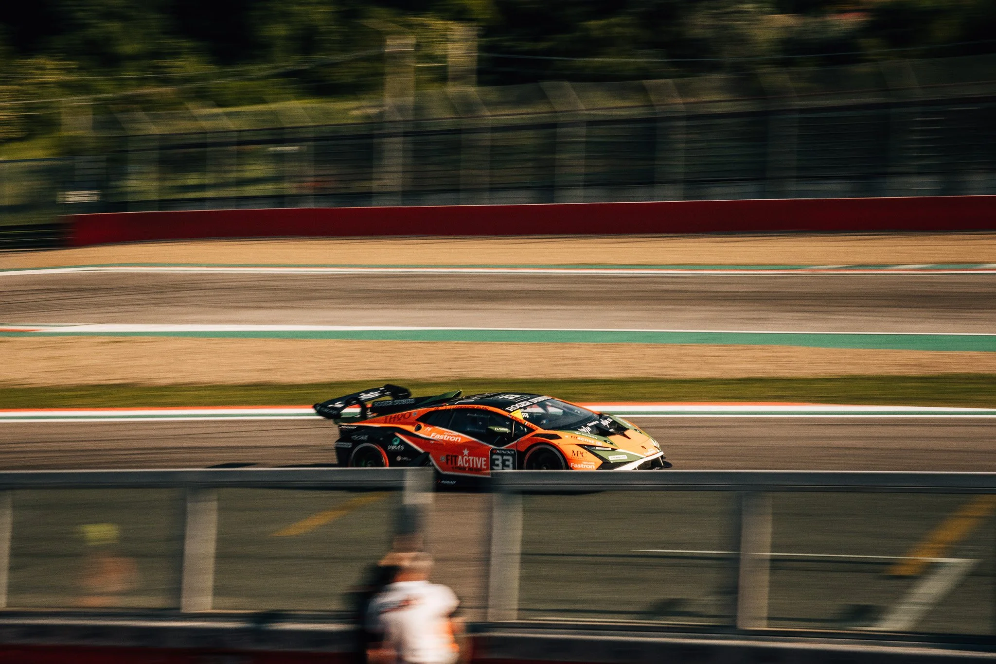 A race car speeding along a racetrack during a race, with blurred background and spectators watching.