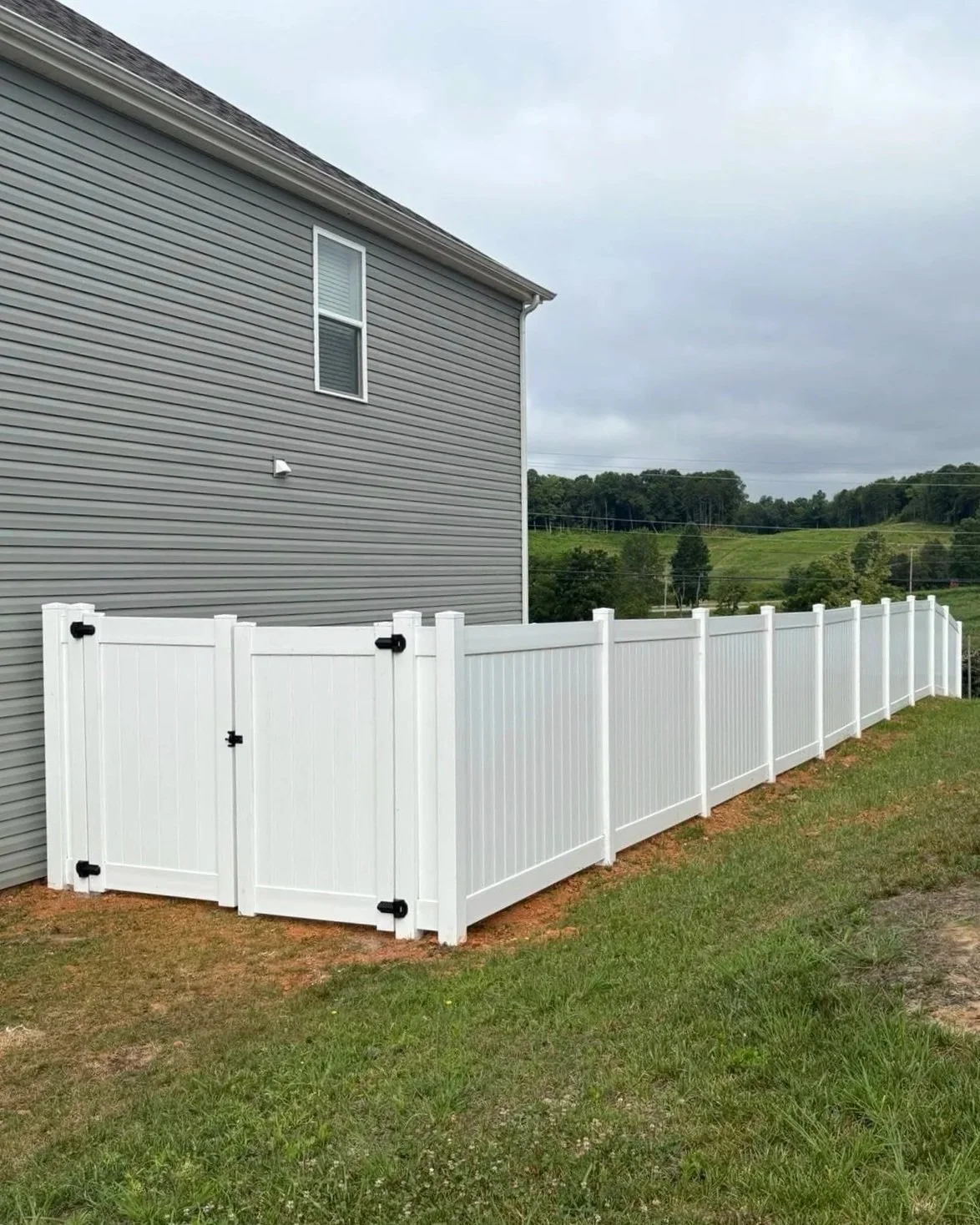 Solid white vinyl privacy fence featuring a double access gate with black hardware, installed by Lane's Fence along a sloped residential side yard.