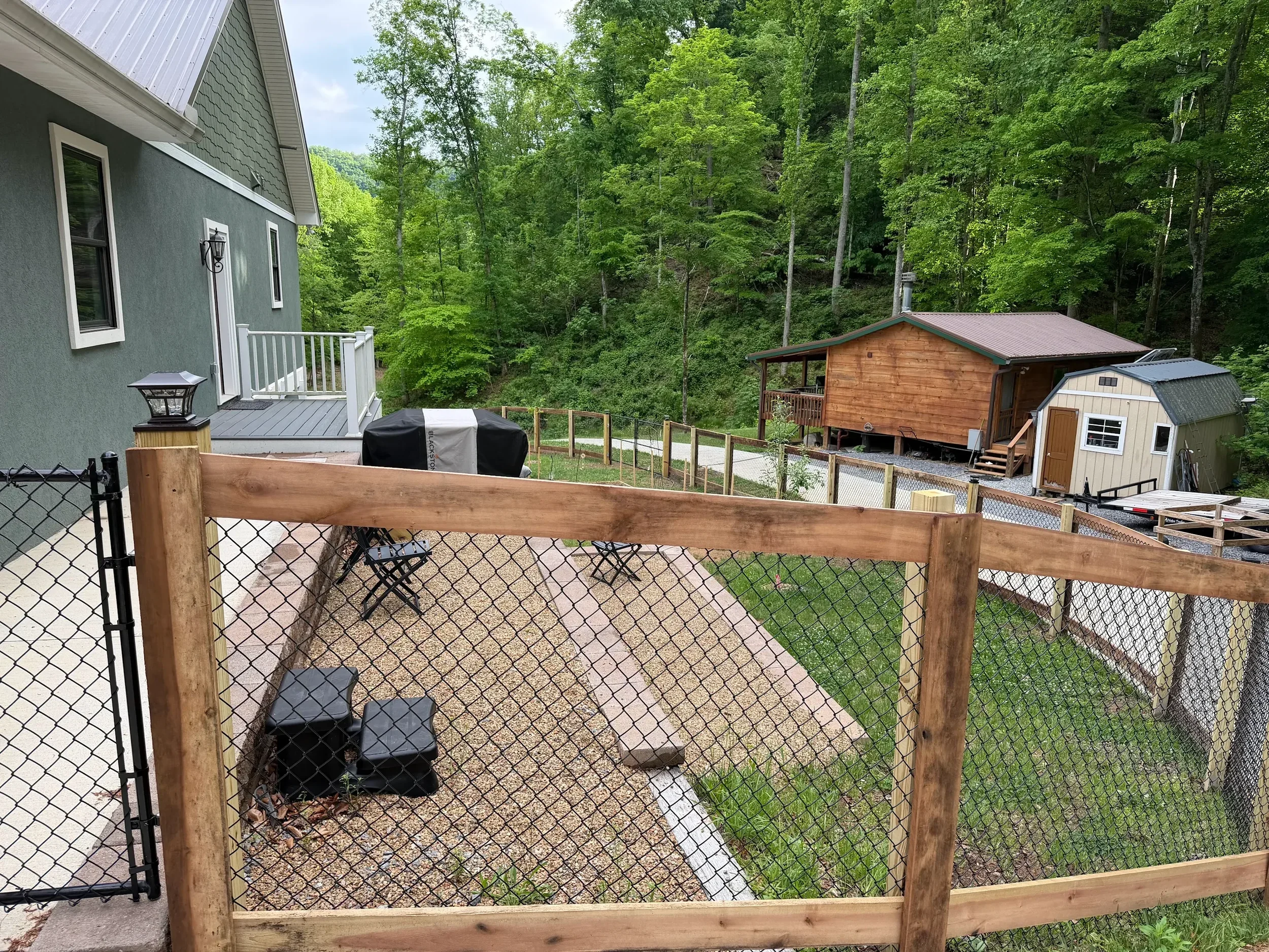 Custom wood frame fence with black chain-link mesh and a matching walk gate installed by Lane's Fence, enclosing a residential backyard and gravel patio area.