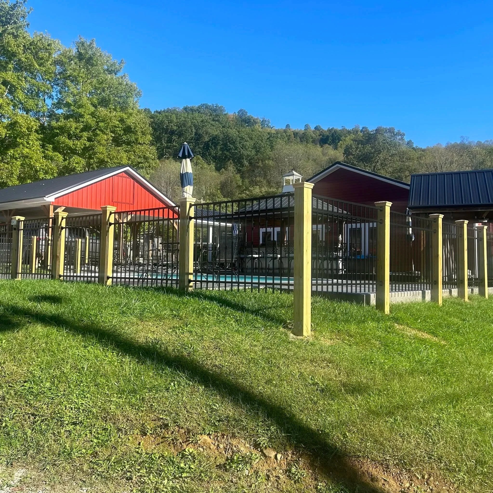 Black ornamental metal pool fence with treated wood posts installed by Lane's Fence, enclosing a residential backyard swimming pool and patio area.