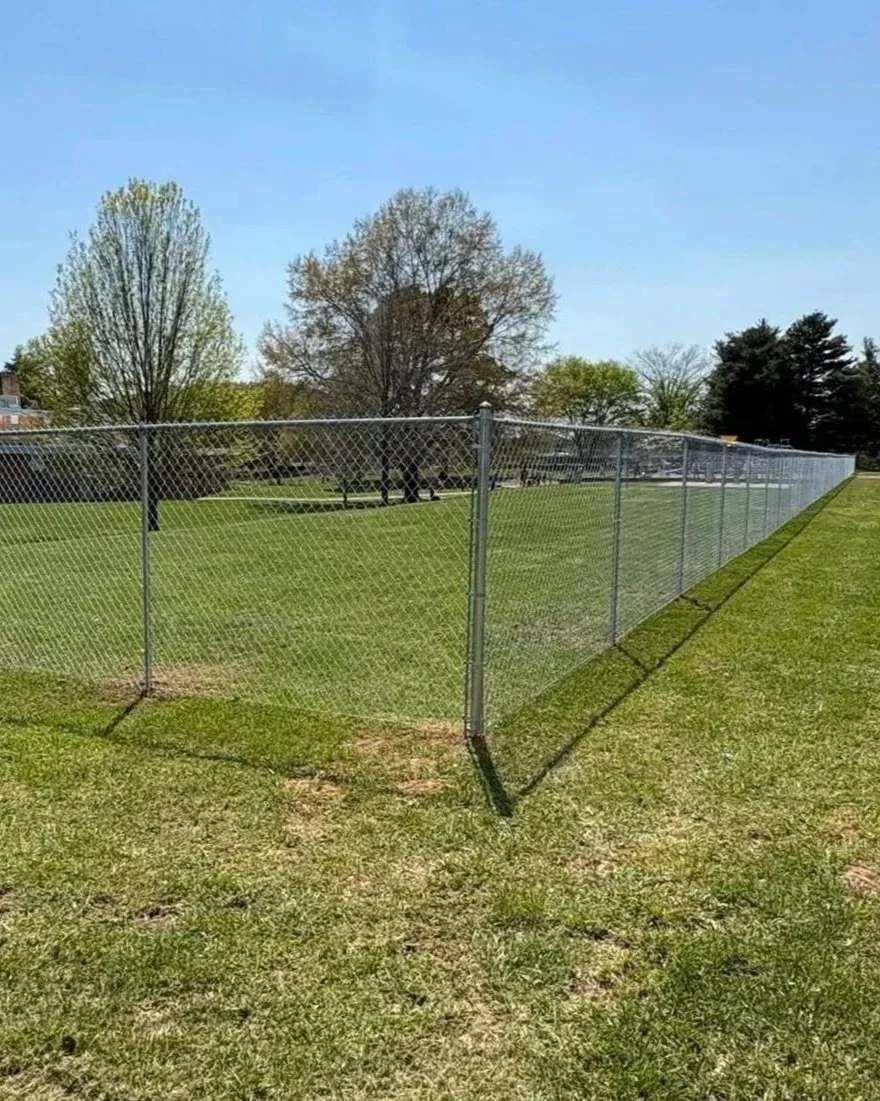 Commercial galvanized chain-link fence installed by Lane's Fence, enclosing a green sports field with a soccer goal in the background.