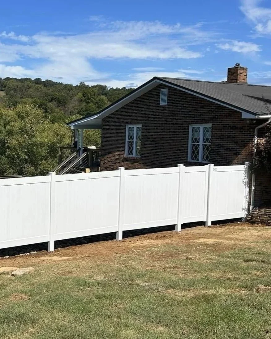 Solid white vinyl privacy fence installed by Lane's Fence, stepped to follow the slope of a residential yard alongside a brick home with a waterfront view.
