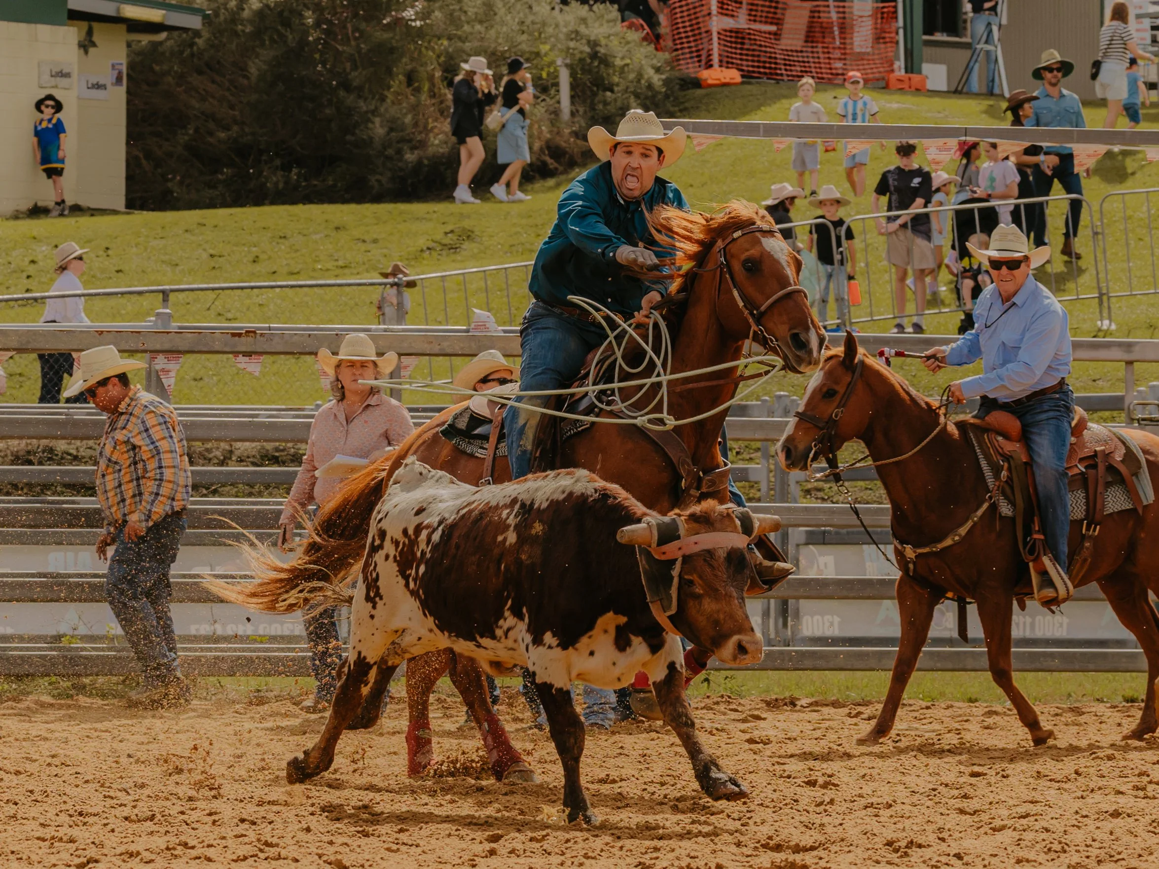 The WESTRN Edit | Western Sports Photography - A man in a cowboy hat and blue shirt riding a horse during a rodeo event with spectators in the background.