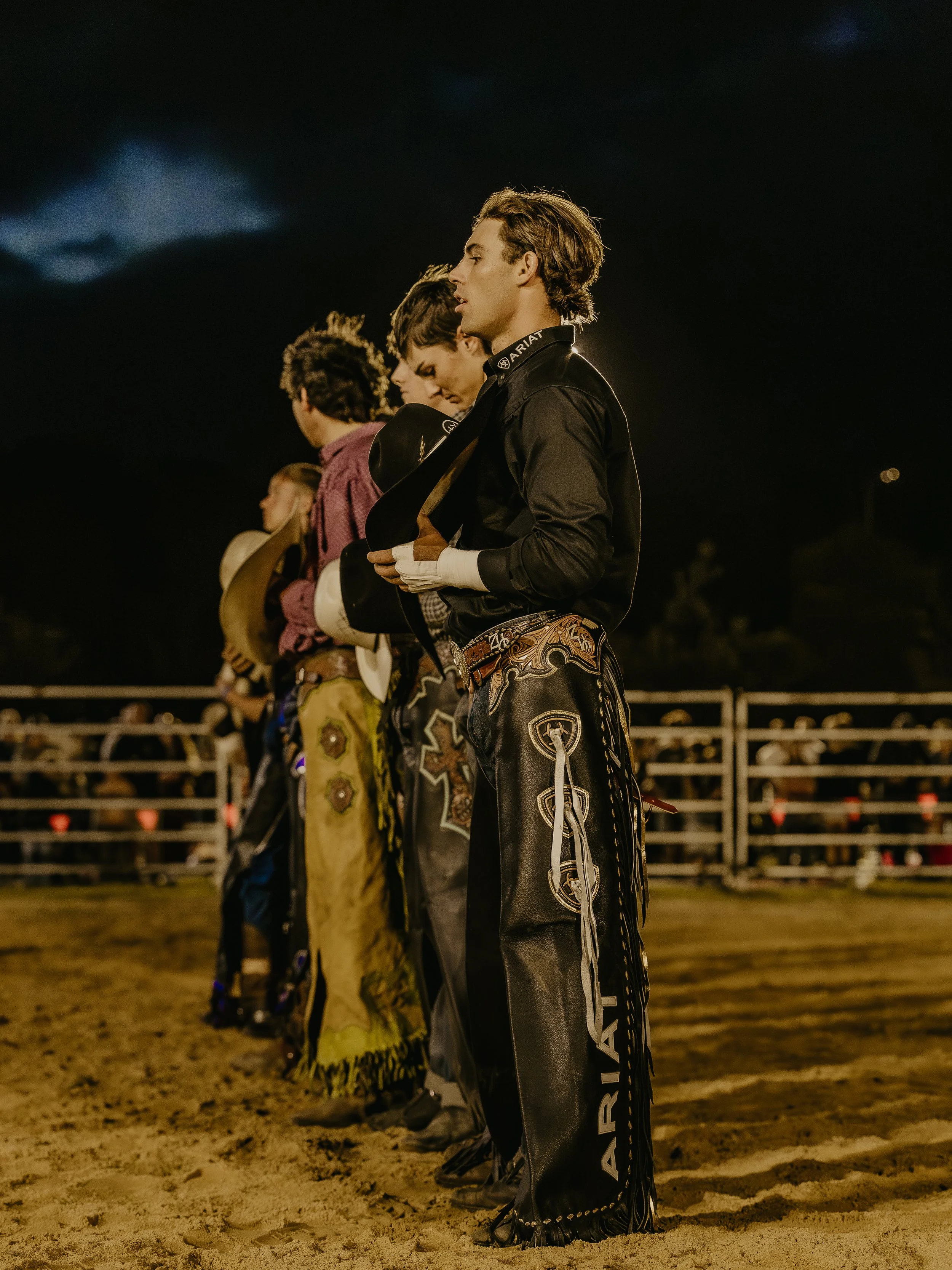 The WESTRN Edit | Western Sports Photography - Young men in Western attire, standing in a line at night, likely preparing for a rodeo event.