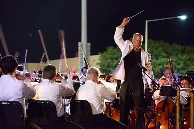 An orchestra performing outdoors at night, with a conductor leading them
