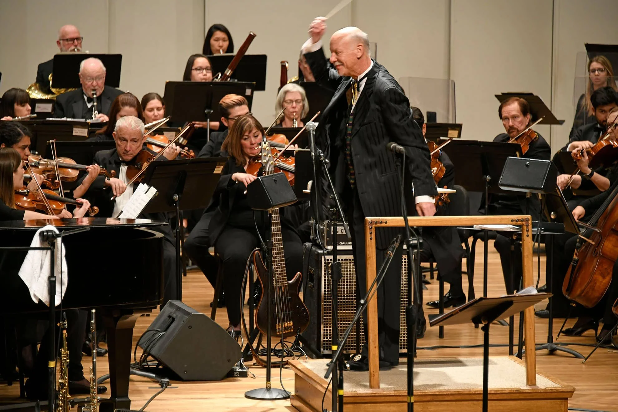 An orchestra performing on stage, featuring musicians playing violins, cellos, and wind instruments, with a conductor guiding them.