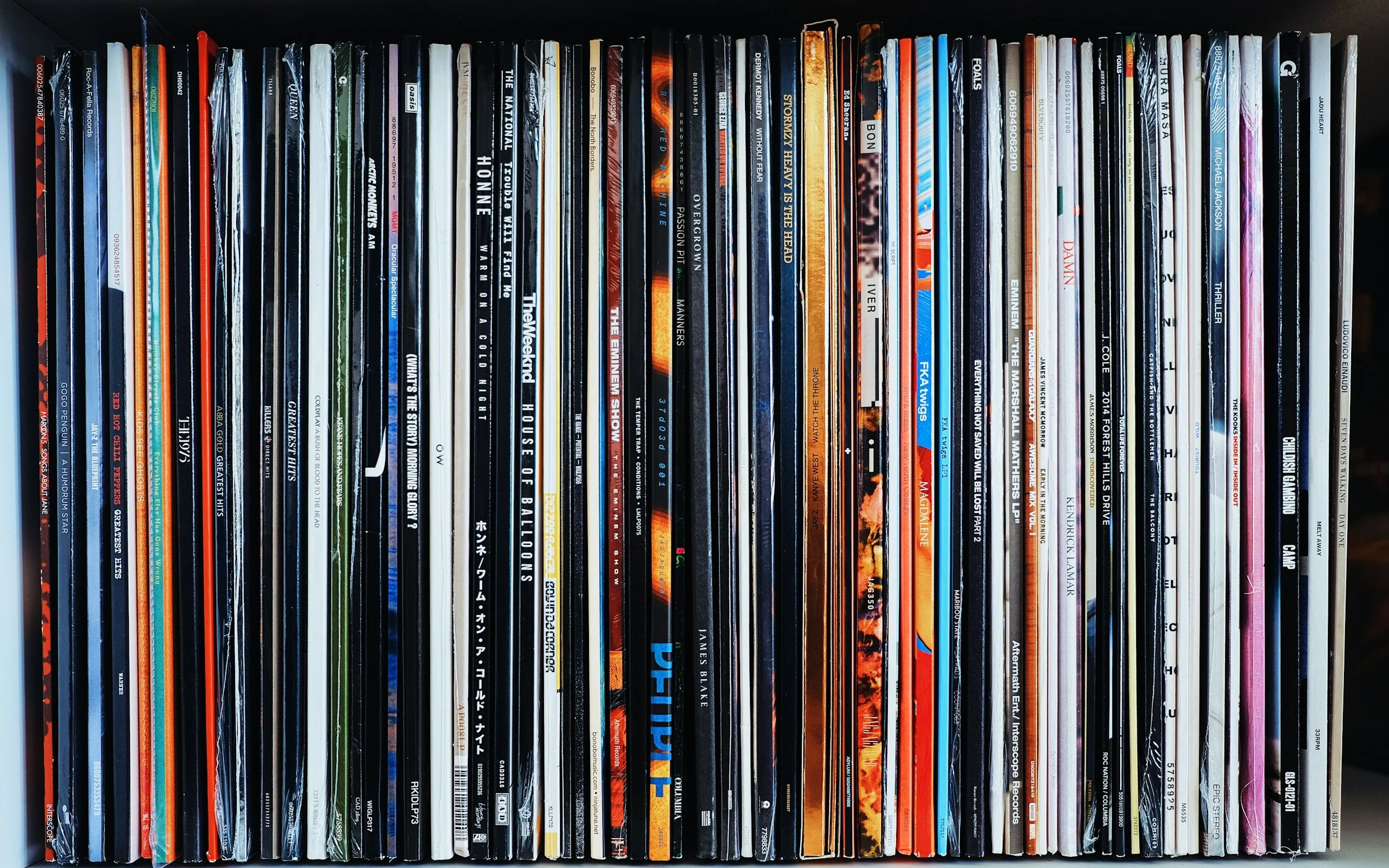 A collection of colorful vinyl records and CD cases arranged vertically on a shelf.