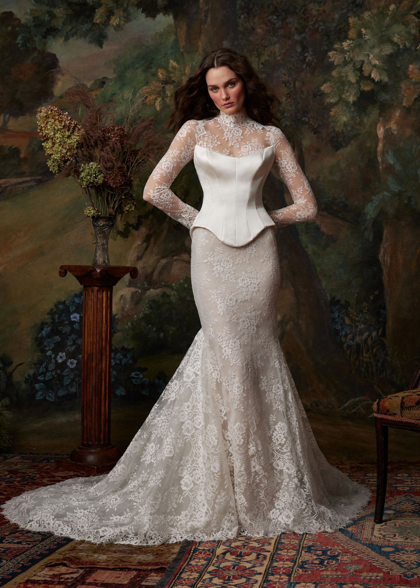 Model wearing an Ines Di Santo long-sleeve lace wedding dress featuring a sheer high neckline layered elegantly beneath a structured white satin corset bodice, flowing into a fitted lace mermaid skirt.