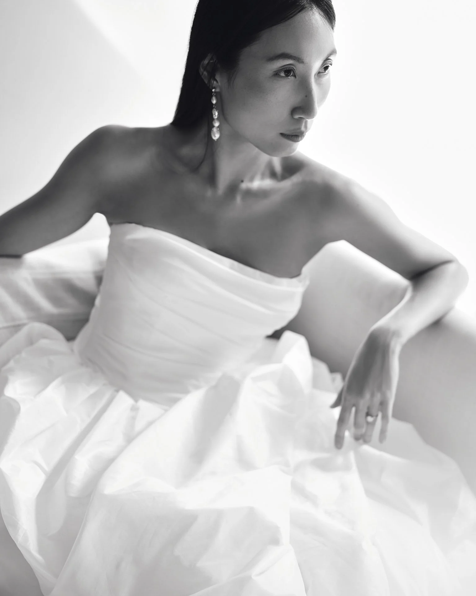 Black-and-white portrait of a bride wearing an elegant Savannah Miller strapless wedding dress featuring a finely ruched bodice and a voluminous gathered skirt, styled with pearl drop earrings.