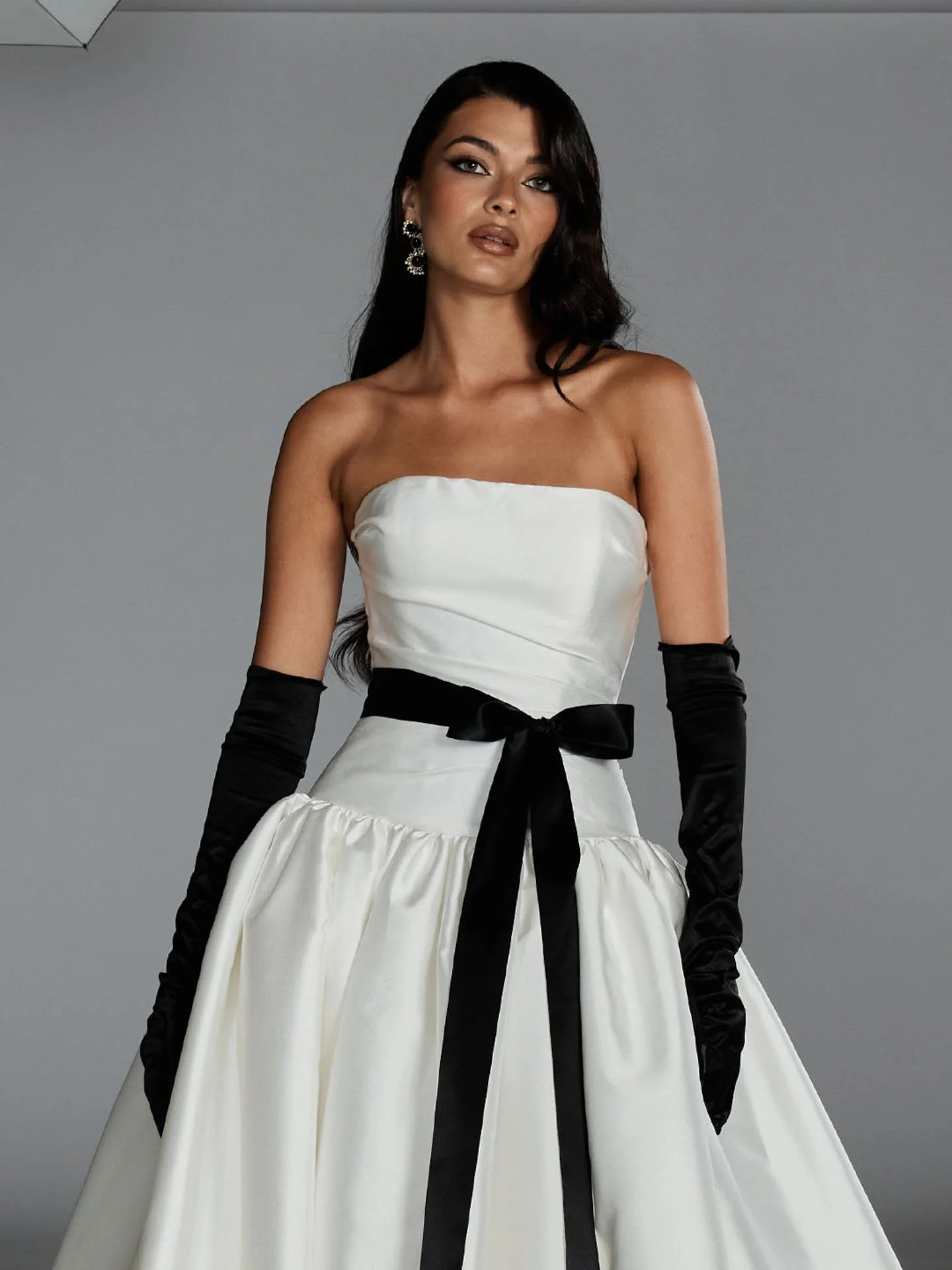 Model wearing a white Evie Young strapless wedding dress styled with a contrasting black ribbon sash tied at the waist and long black satin opera gloves.