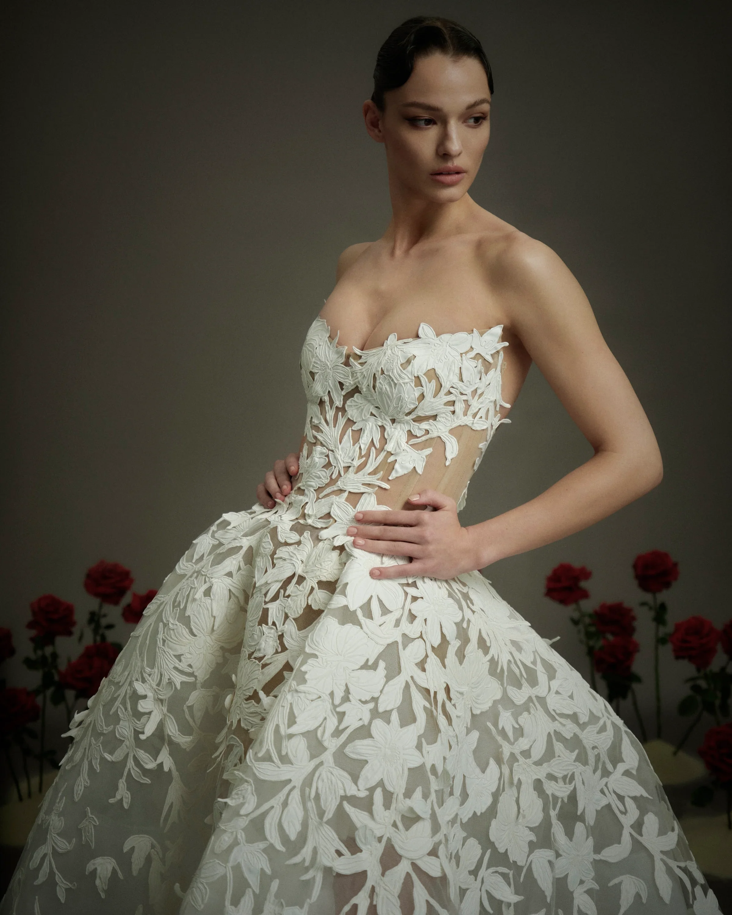 Close-up of a model wearing a Nicole and Felicia strapless wedding dress highlighting a sheer corset bodice with a sweetheart neckline and bold, oversized floral and leaf appliqués.