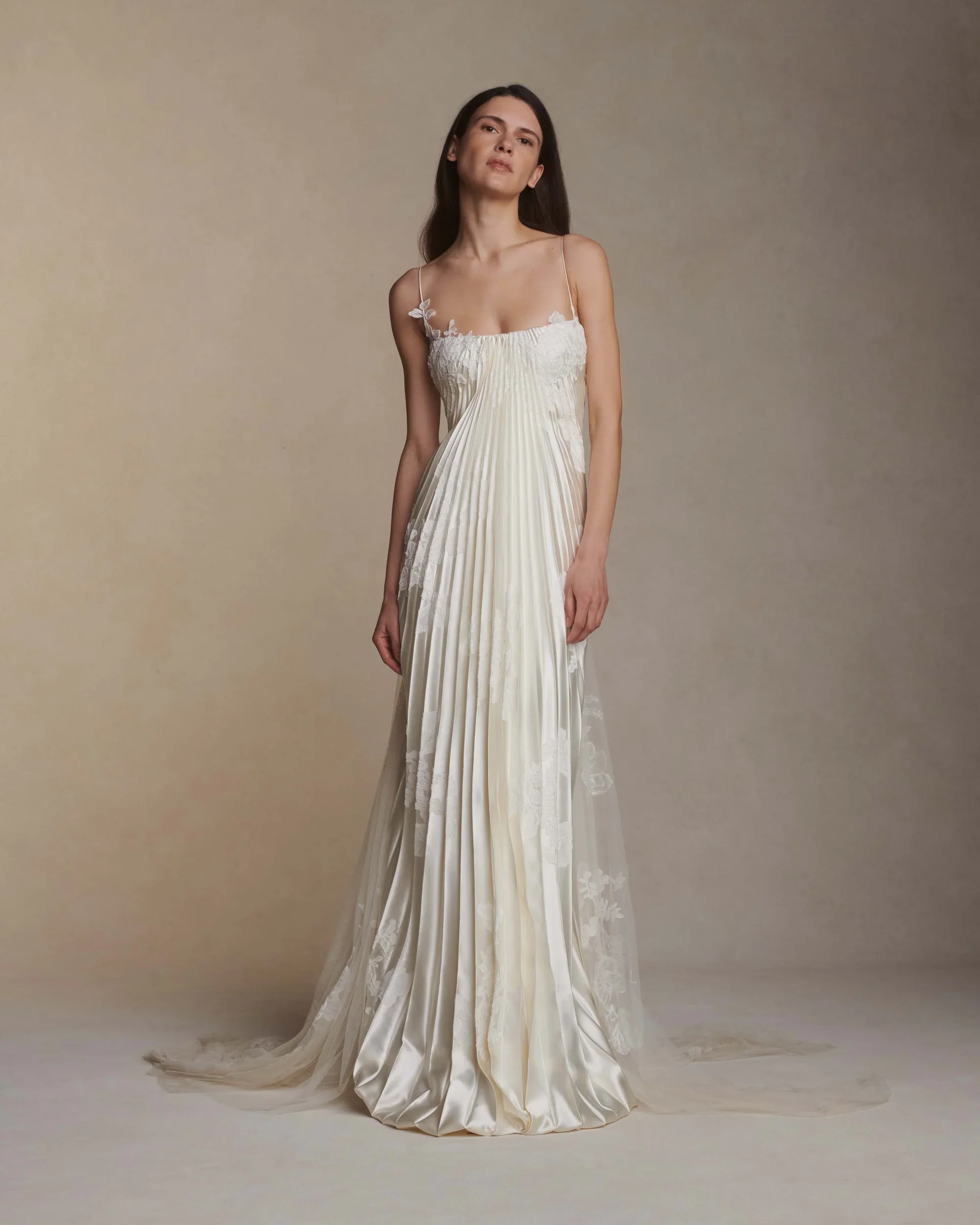 Model wearing a Danielle Frankel silk wedding dress with delicate spaghetti straps, featuring intricate all-over vertical pleating and beautiful sheer floral lace overlays.