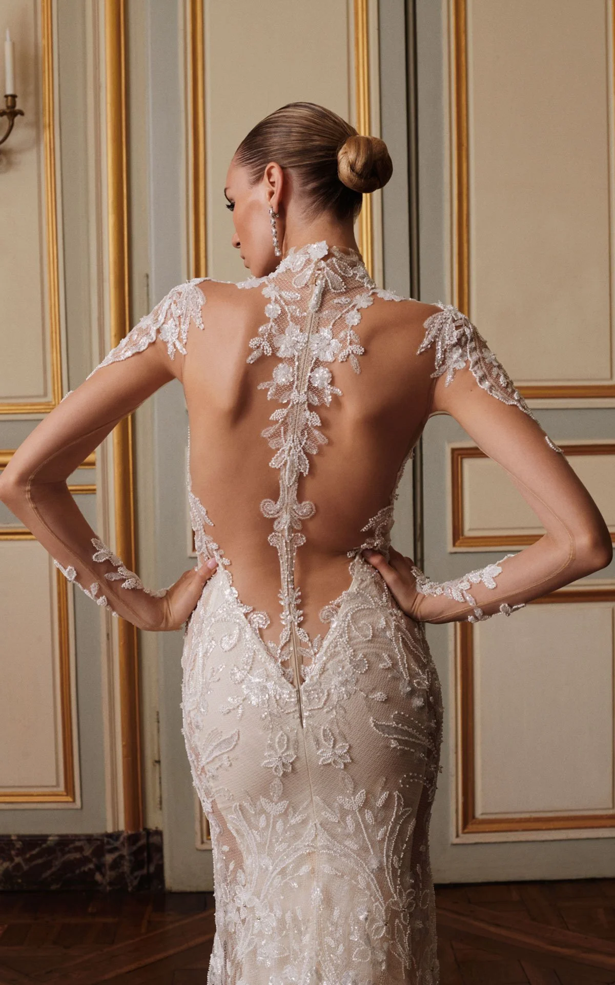 Back view of a model wearing a Galia Lahav Couture long-sleeve wedding dress, showcasing a sheer illusion back with elaborate beaded floral lace appliqués tracing down the spine.