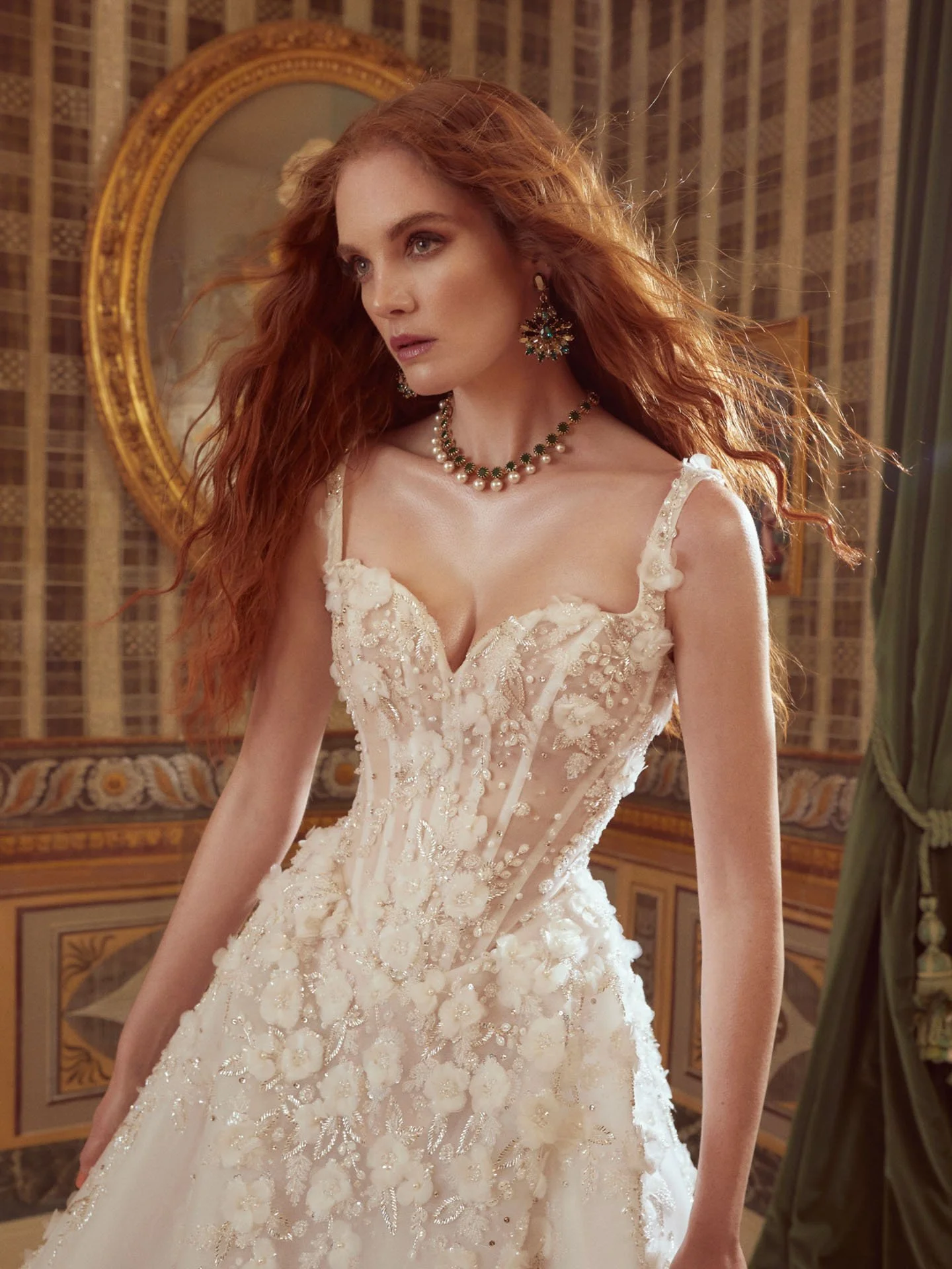 Close-up of a model wearing a Galia Lahav Couture wedding dress featuring a plunging sweetheart corset bodice adorned with heavily beaded 3D floral appliqués, styled with an emerald and pearl necklace.