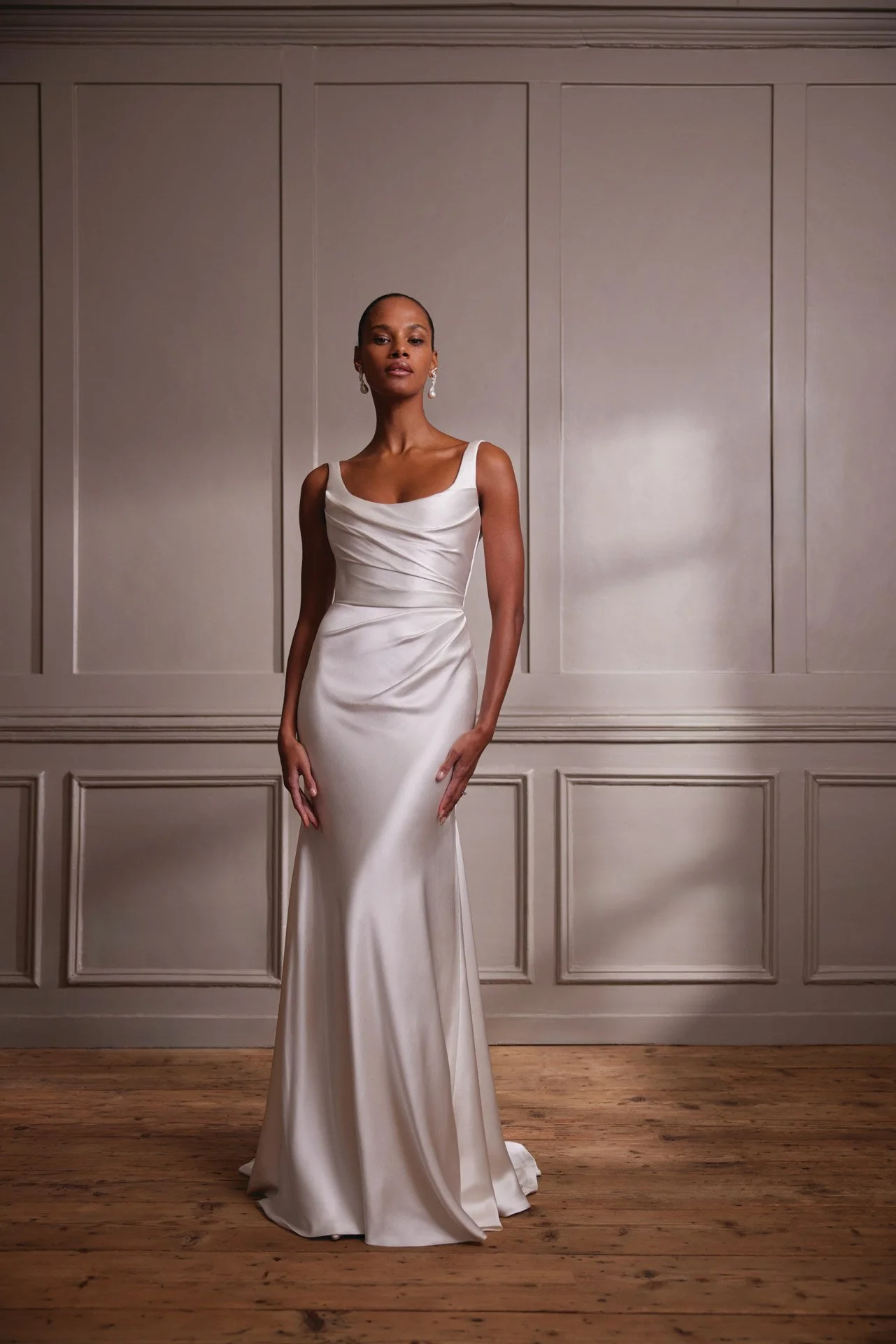 Model wearing an elegant Savannah Miller satin sheath wedding dress featuring wide shoulder straps, a classic scoop neckline, and intricate diagonal draping across the fitted bodice and waist.